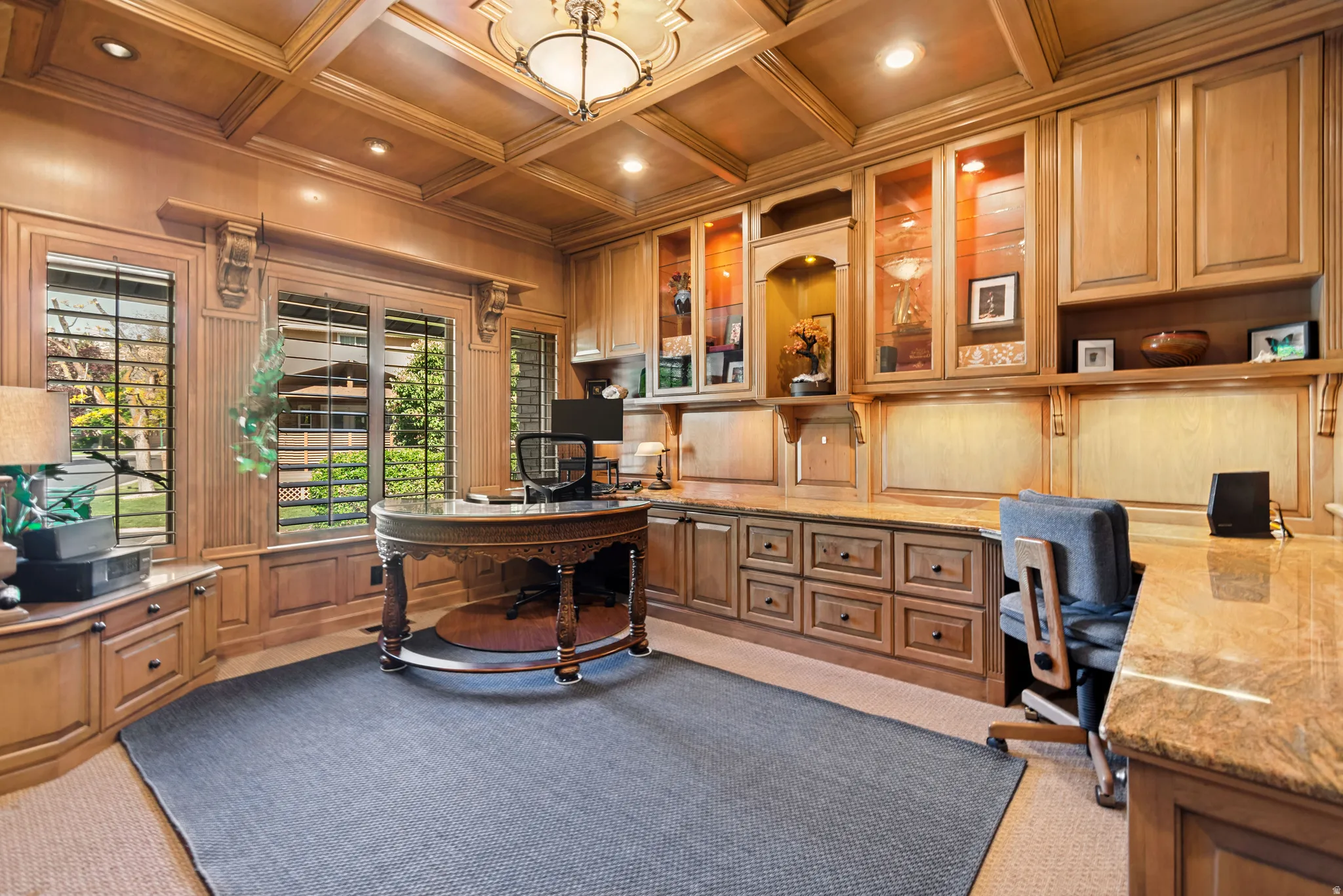 Room featuring extensive built-in cabinetry, coffered ceiling with recessed lighting, integrated display shelving, and substantial granite countertops
