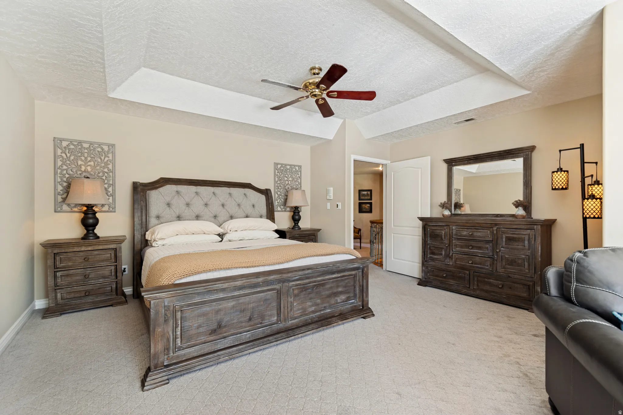 Neutral-toned room featuring a tray ceiling with a ceiling fan, light-colored carpeting, and a doorway opening to an interior space