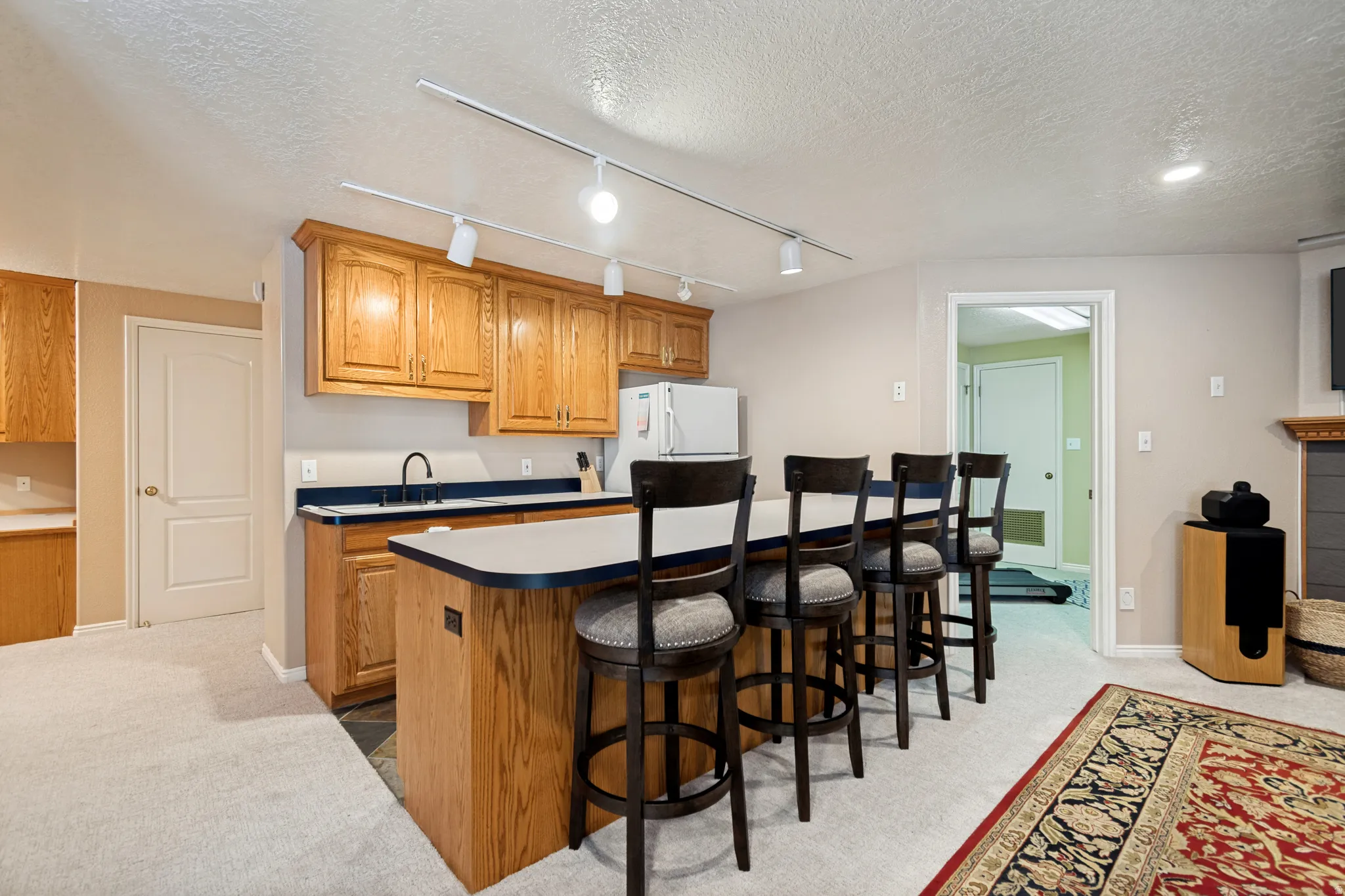 Kitchenette featuring wood cabinetry, a white countertop with a black undermount sink, and track lighting