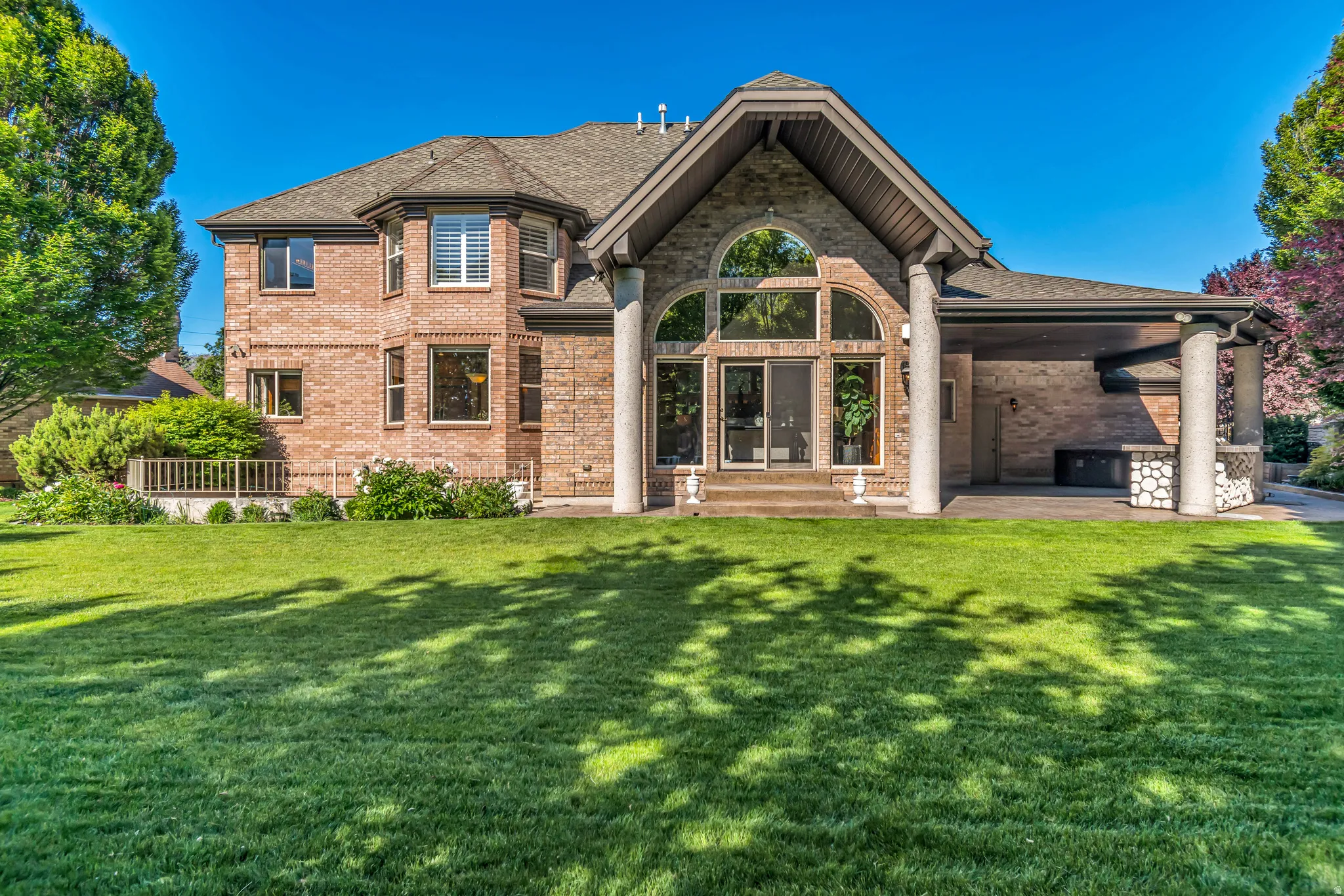 Brick exterior residence featuring a covered patio, expansive lawn, and a multi-level deck
