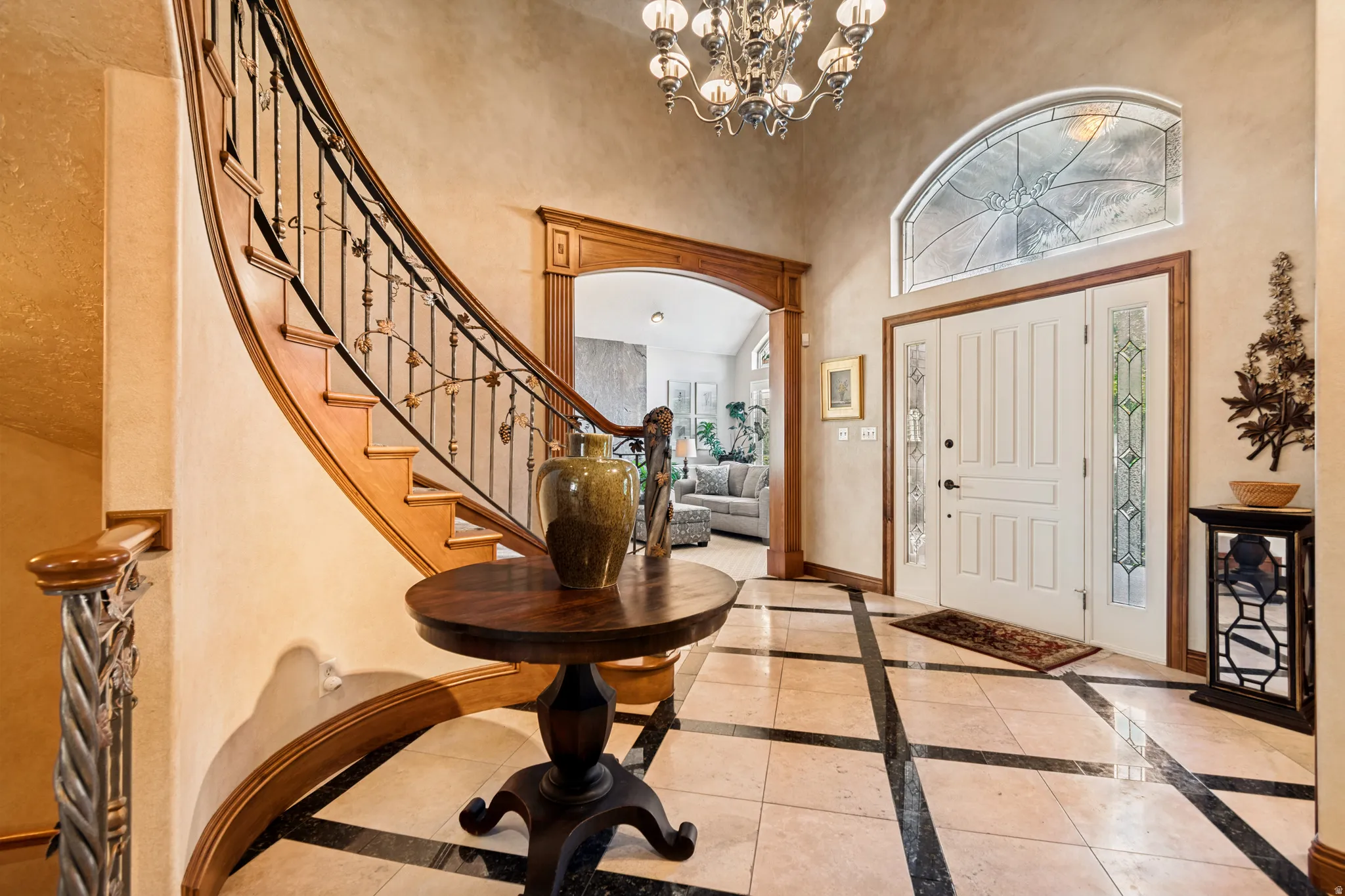 Grand entryway featuring a curved staircase with ornate ironwork railing, wood-finish treads, and a statement chandelier