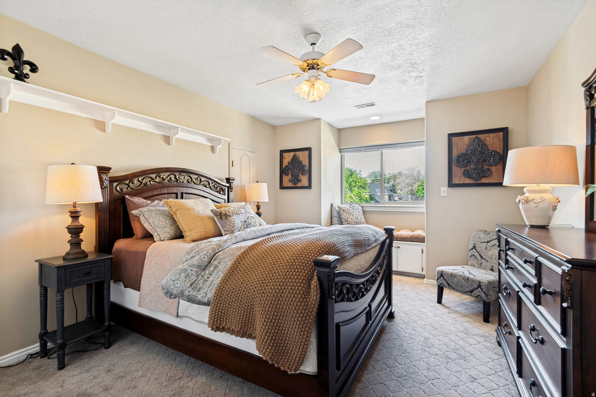Spacious room featuring neutral wall tones, textured carpeting, a ceiling fan with integrated lighting, a built-in window bench with storage, and decorative shelving