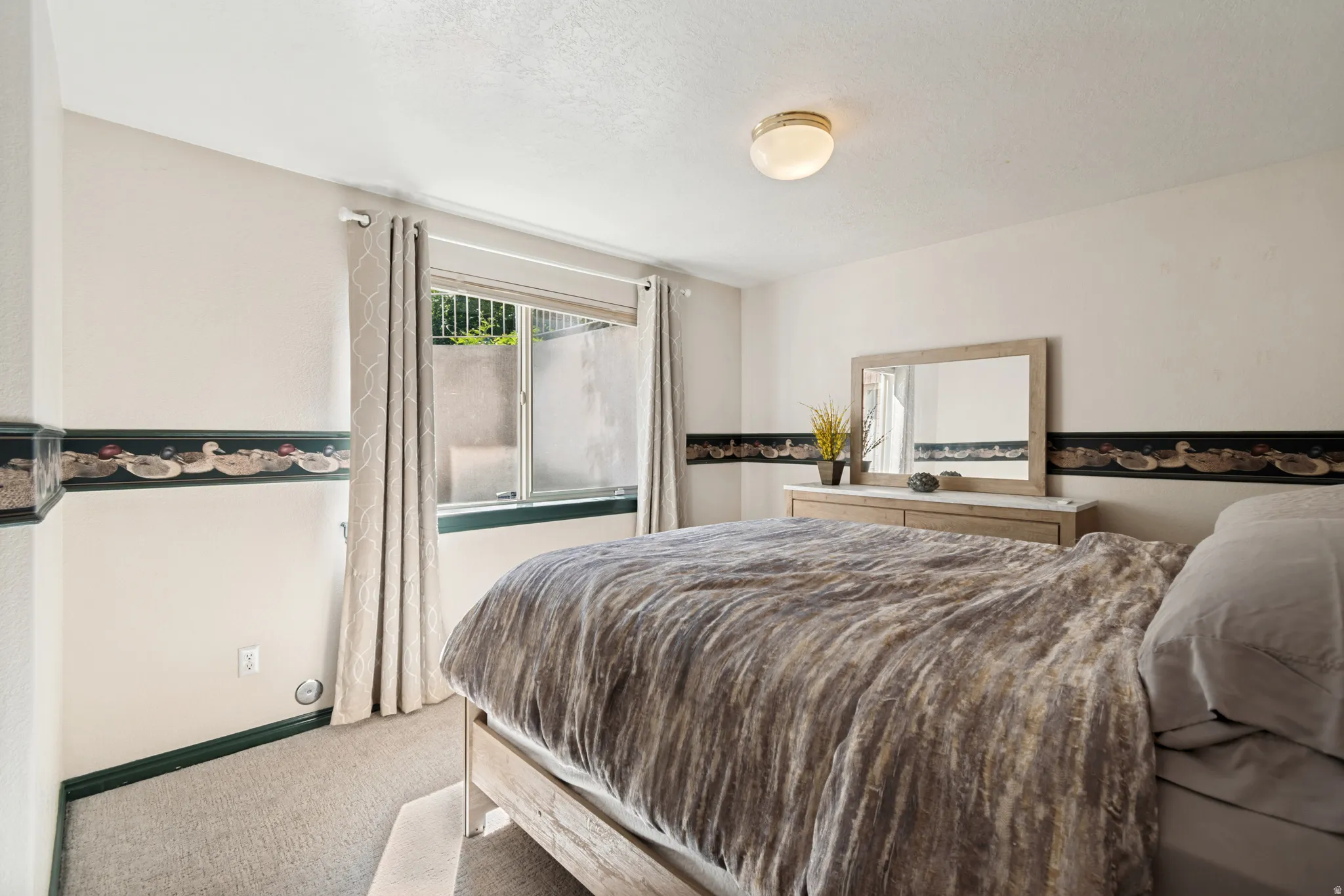 Carpeted room with a wall-mounted light fixture and a window featuring vertical blinds
