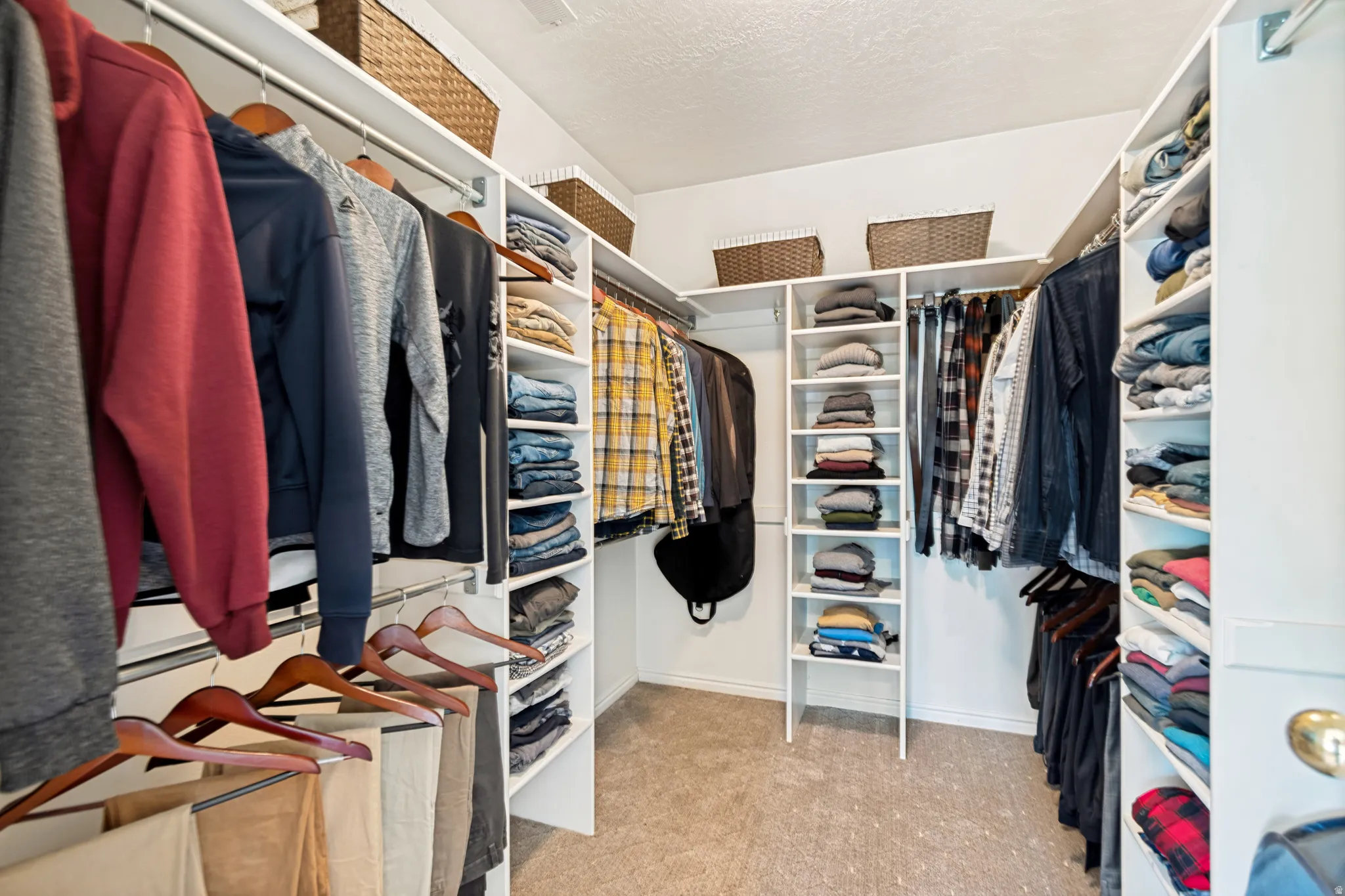 Walk-in closet featuring built-in white shelving, multiple hanging rods, and carpet flooring