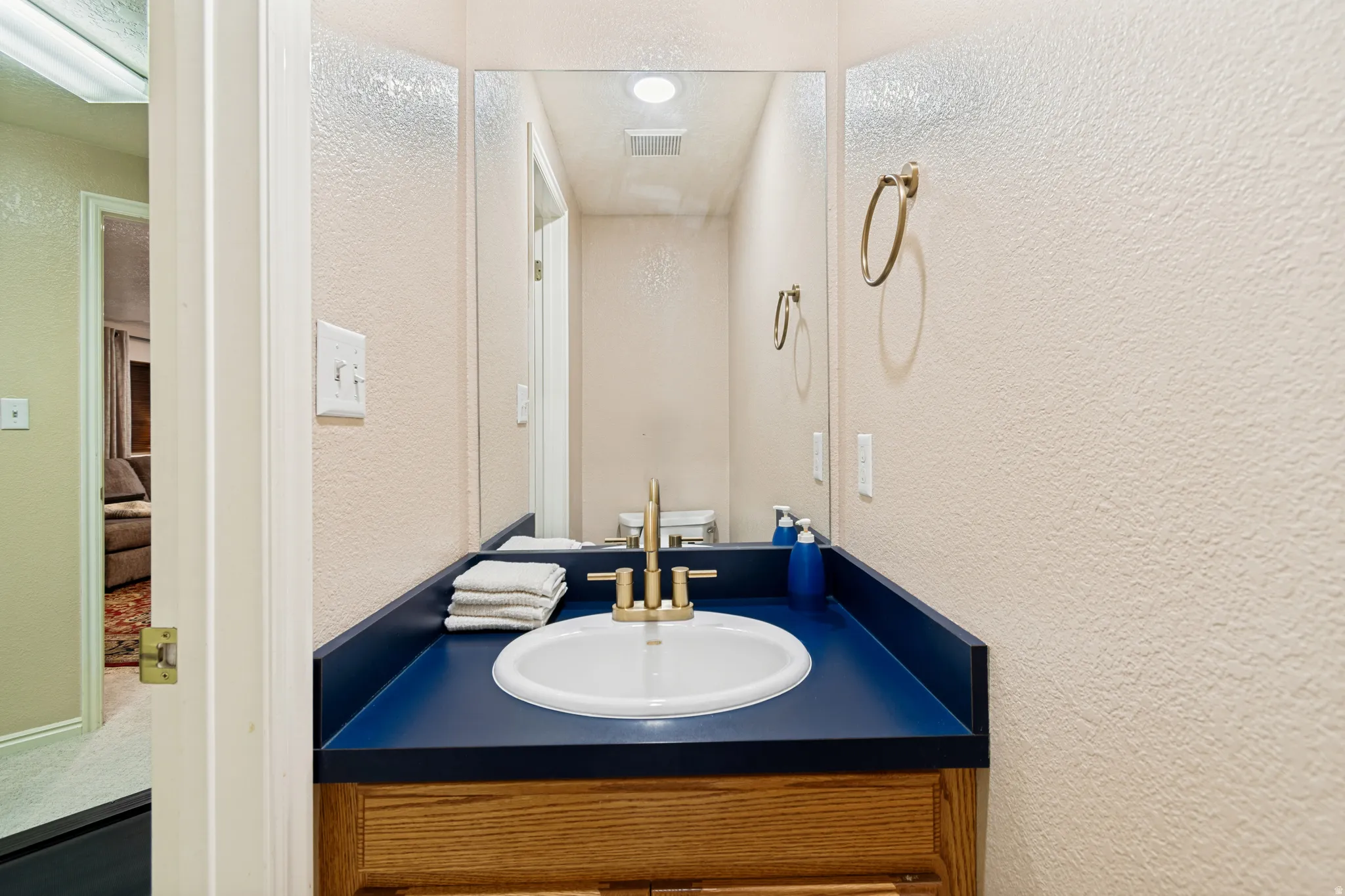 Bathroom vanity featuring a white oval sink, brass-finish faucet, and a blue countertop