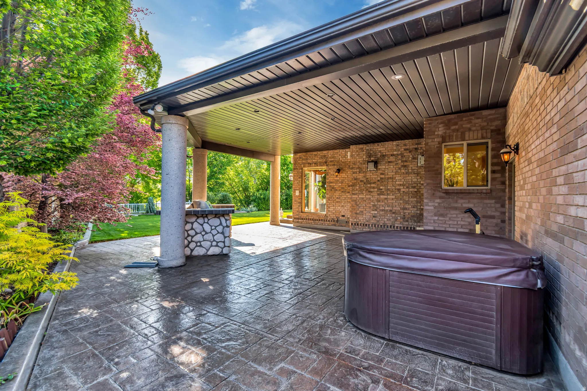 Covered patio featuring stamped concrete flooring, a built-in outdoor kitchen with stone accents, a spa, and brick exterior walls