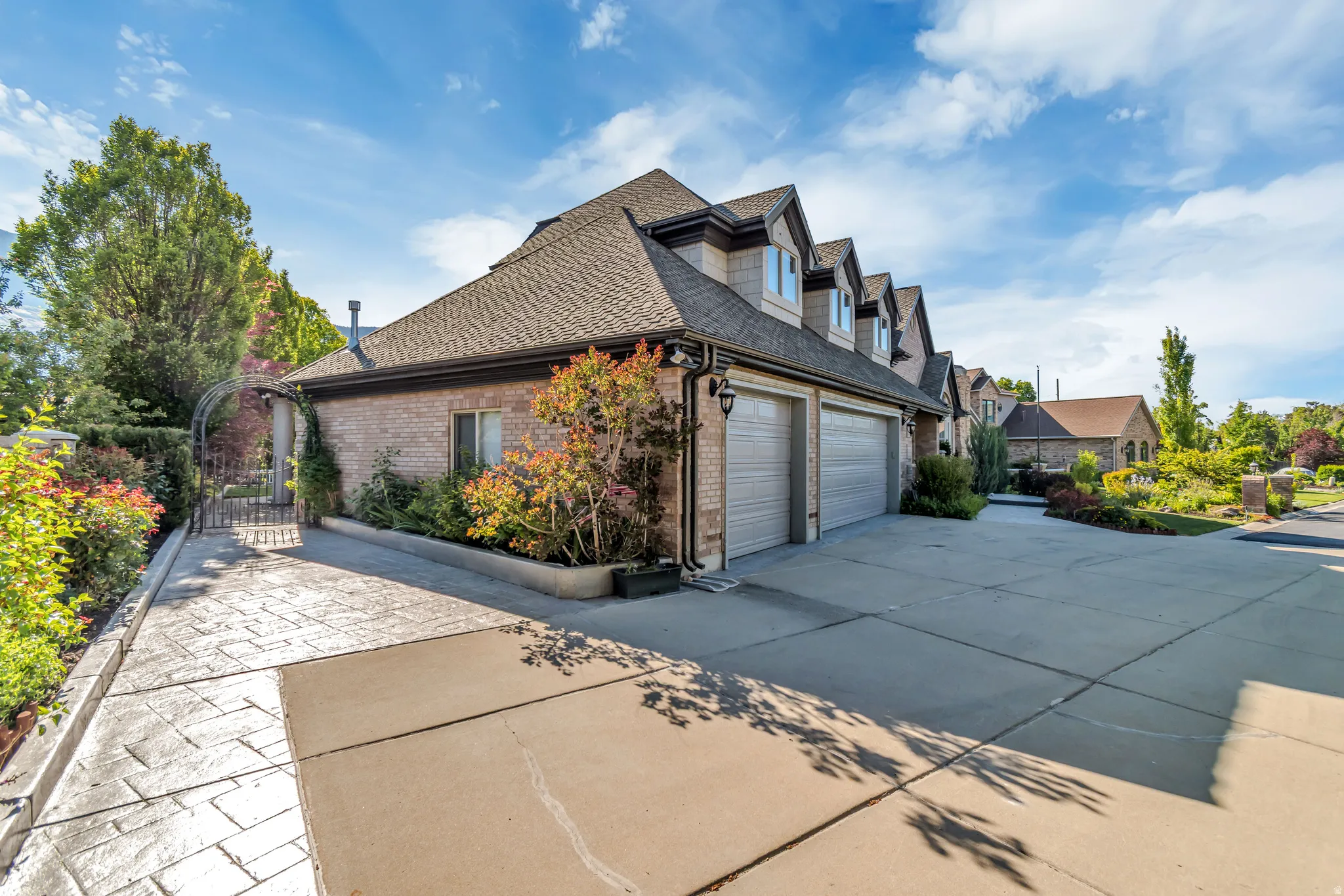Brick and stone exterior featuring multiple garage bays, a patterned concrete driveway, and dormer windows
