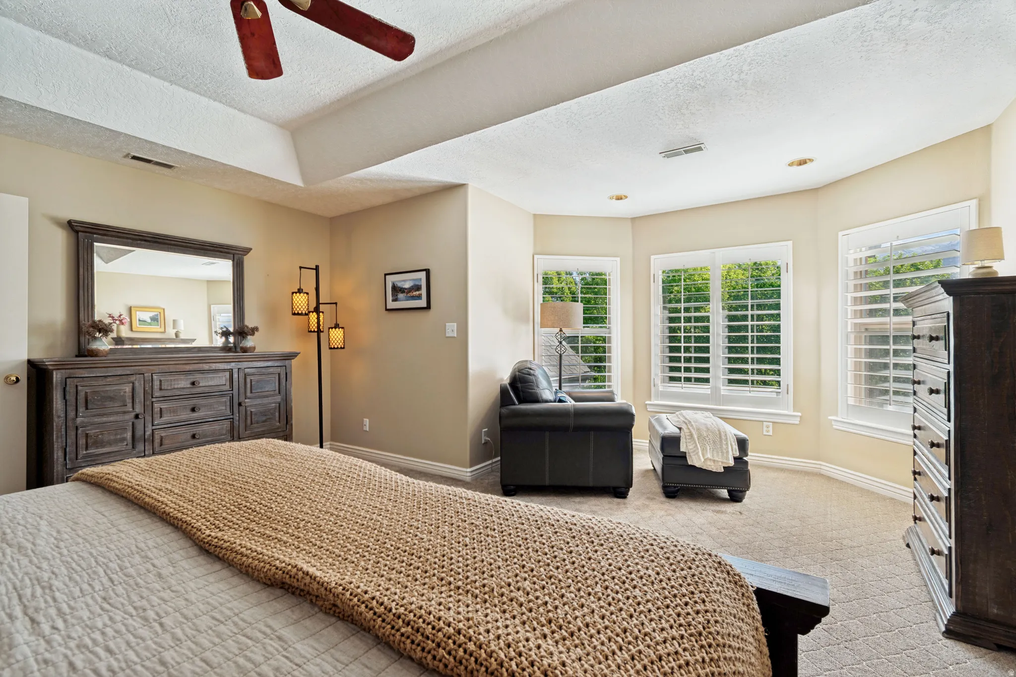 Carpeted room featuring a ceiling fan, recessed lighting, and bay windows with plantation shutters