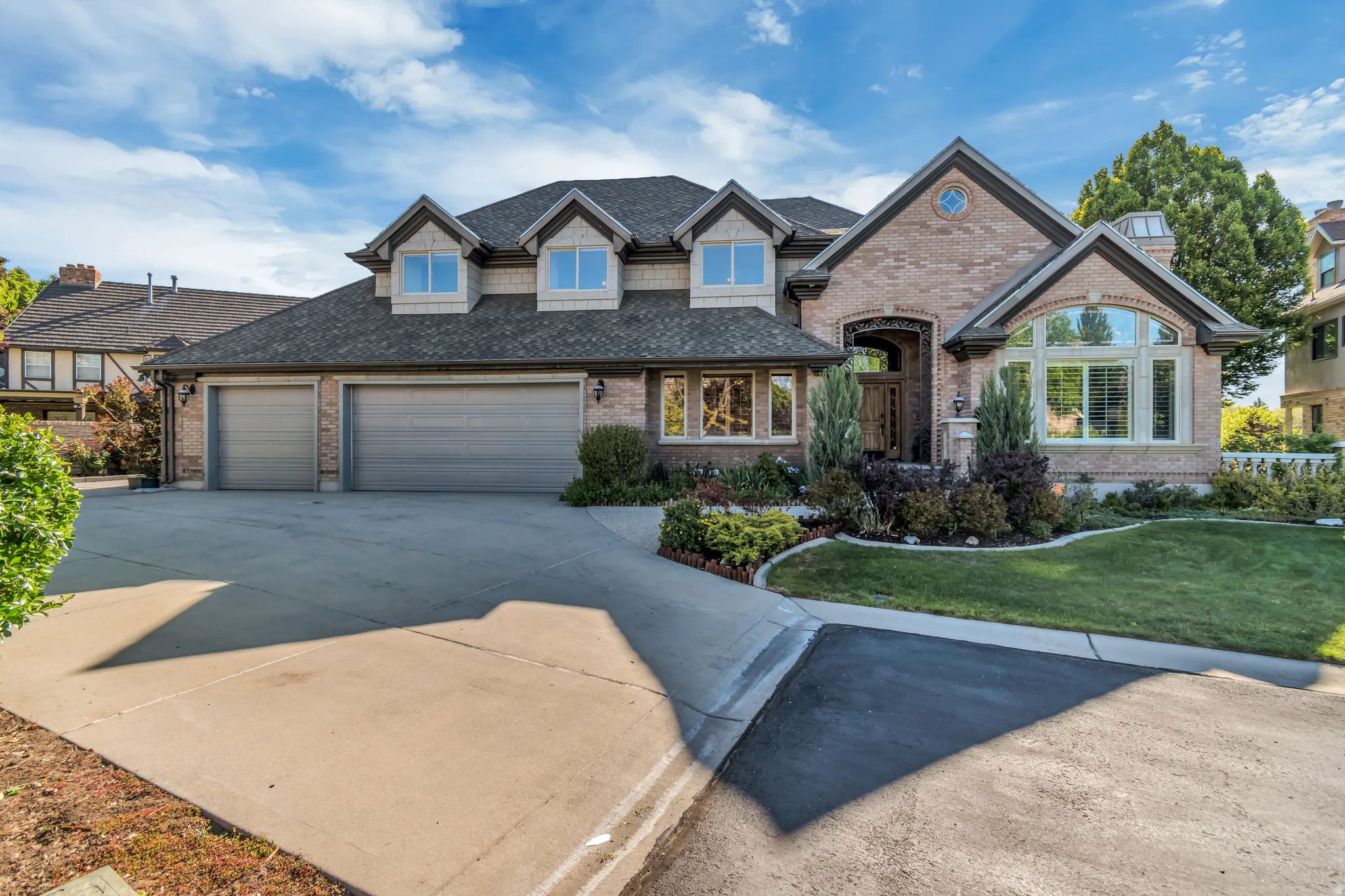 Brick exterior featuring a multi-car garage, dormer windows, arched entry, and an arched window