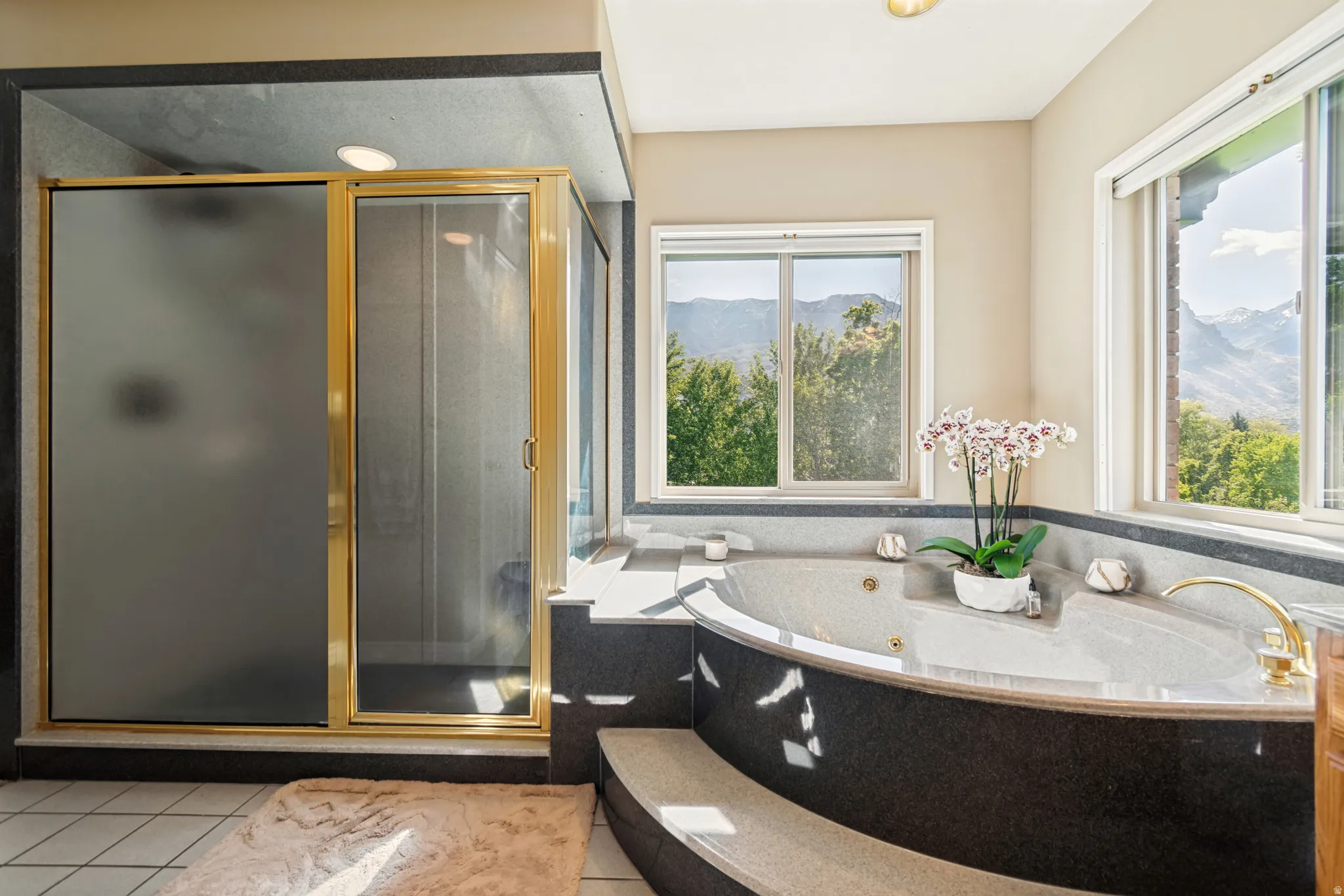 Soaking tub with integrated steps, surrounded by dark-toned stone-finish tiling, and featuring gold-tone fixtures