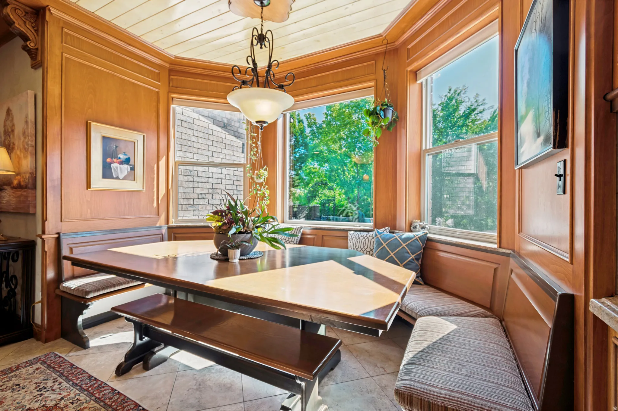 Bay window dining nook featuring built-in bench seating with striped cushions, wood-paneled walls, and a multi-pane pendant light fixture
