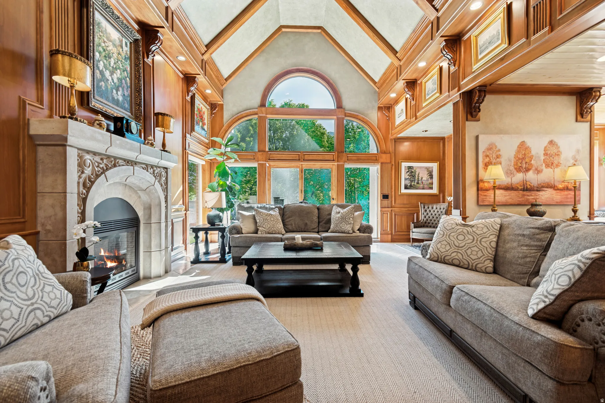 Vaulted ceiling with exposed wood beams and paneling, stone-surround fireplace, arched window, and full-height glass patio doors