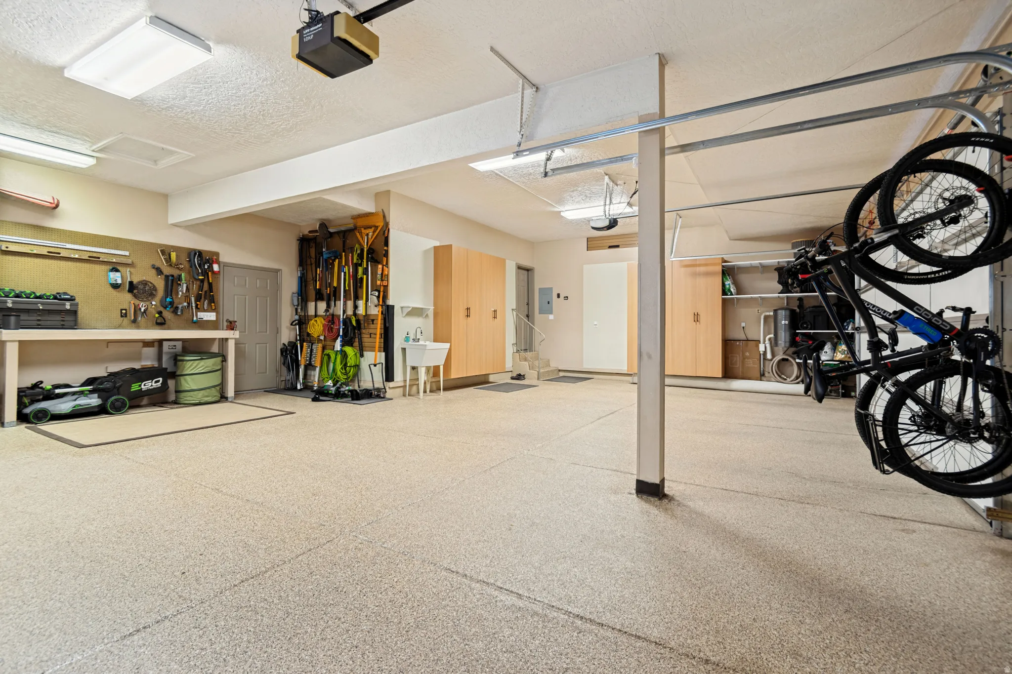 Spacious garage featuring a durable epoxy floor, built-in cabinetry for extensive storage, a functional workbench, and overhead fluorescent lighting