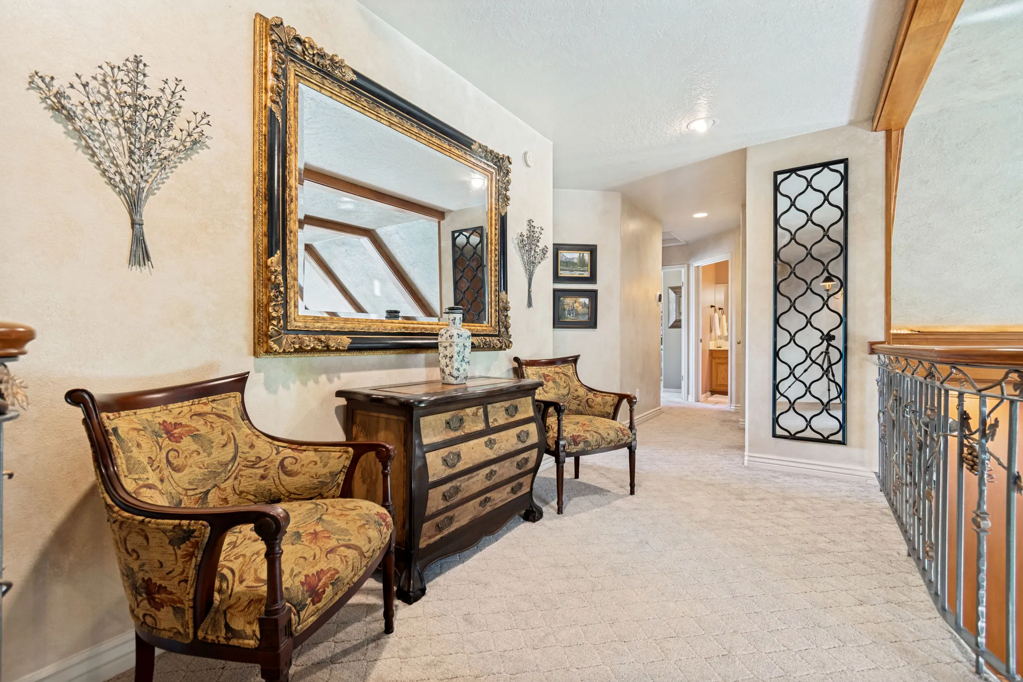 Carpeted hallway featuring a decorative metal railing, wood-beam accents, a built-in wall niche with metal artwork, and an ornate framed mirror