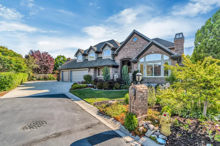 Brick facade residence featuring a multi-car driveway, mature landscaping, arched windows, and a prominent brick chimney