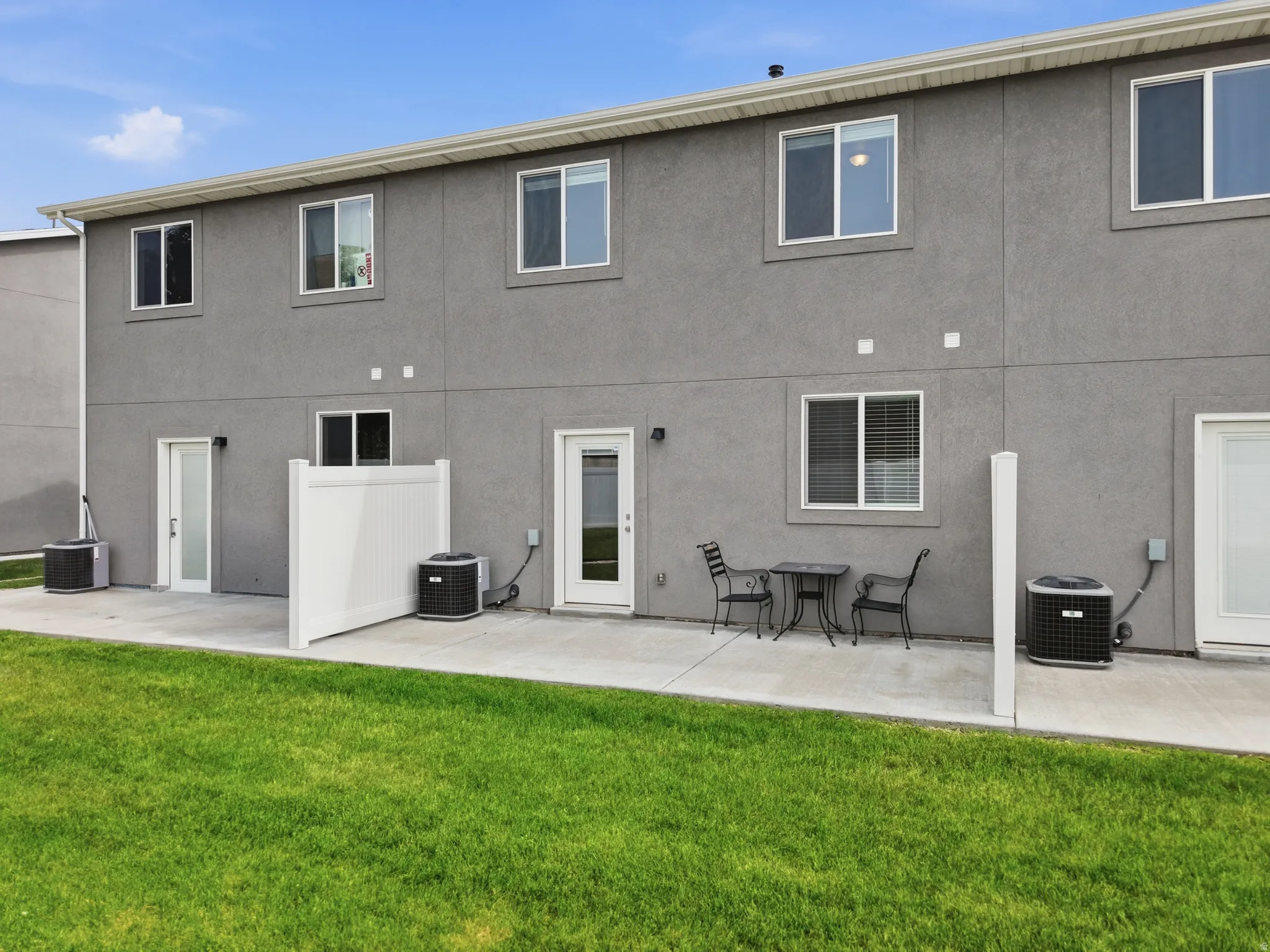 Exterior patio area featuring a concrete slab, a partial privacy fence, and a vibrant green lawn