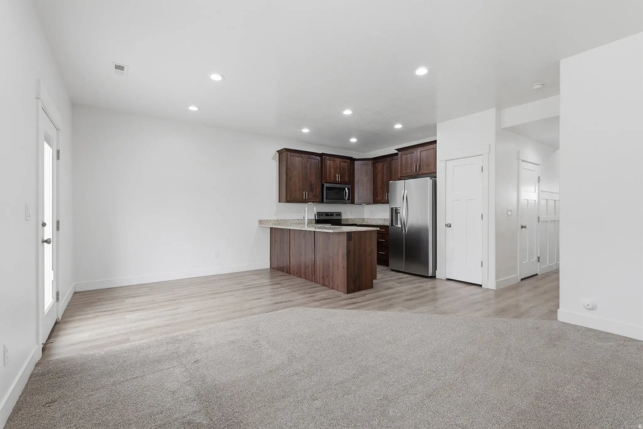 Open-concept living area featuring a kitchen with dark wood-finish cabinetry, stainless steel appliances, and a peninsula with a light-toned countertop