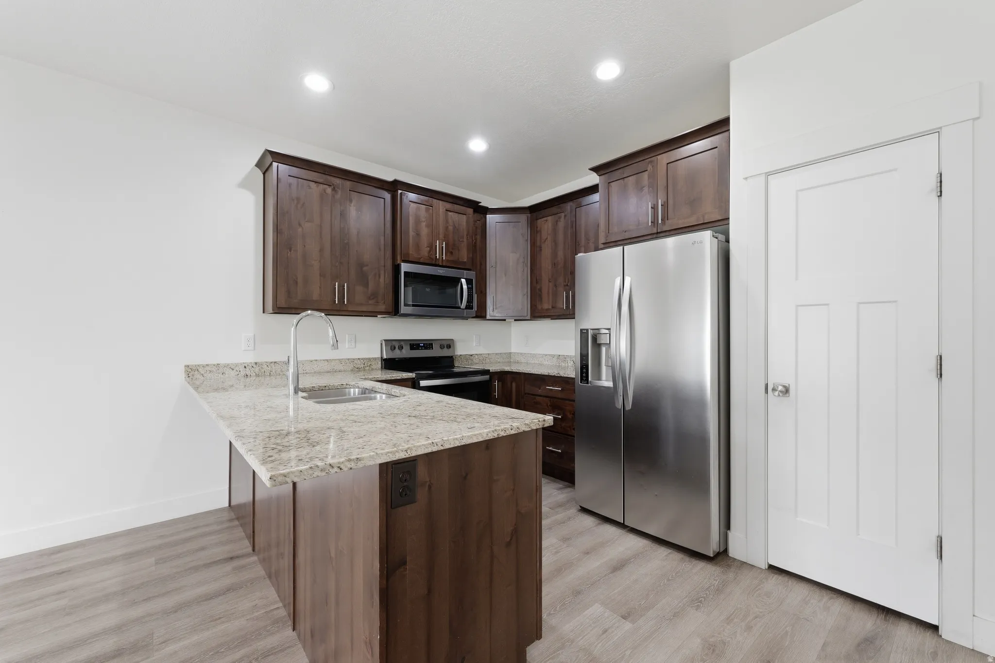 Kitchen featuring wood-finish cabinetry, light-toned granite countertops, and stainless steel appliances including a side-by-side refrigerator, microwave, and range
