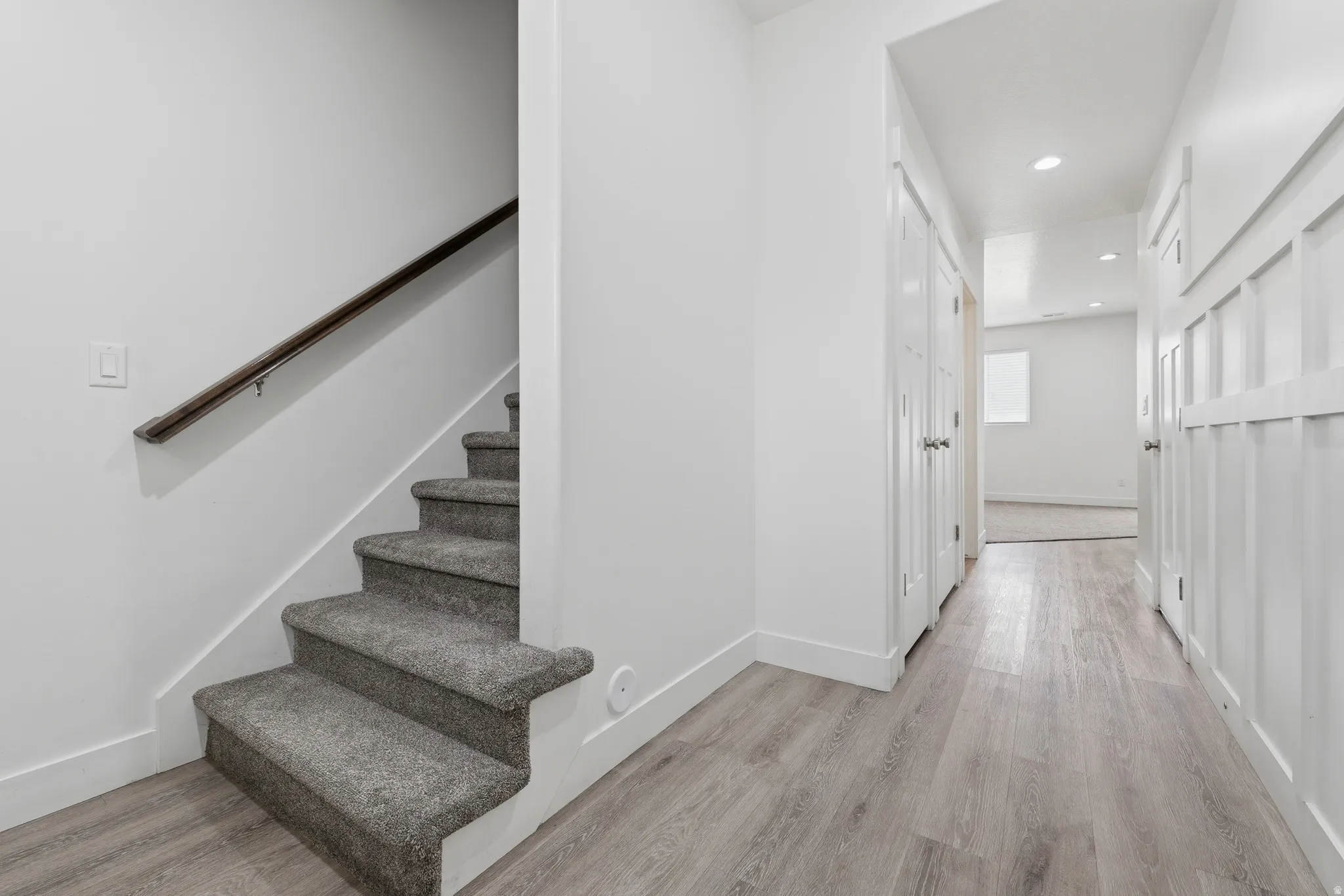 Staircase with gray carpeted treads and a dark wood handrail, complemented by light wood-finish flooring