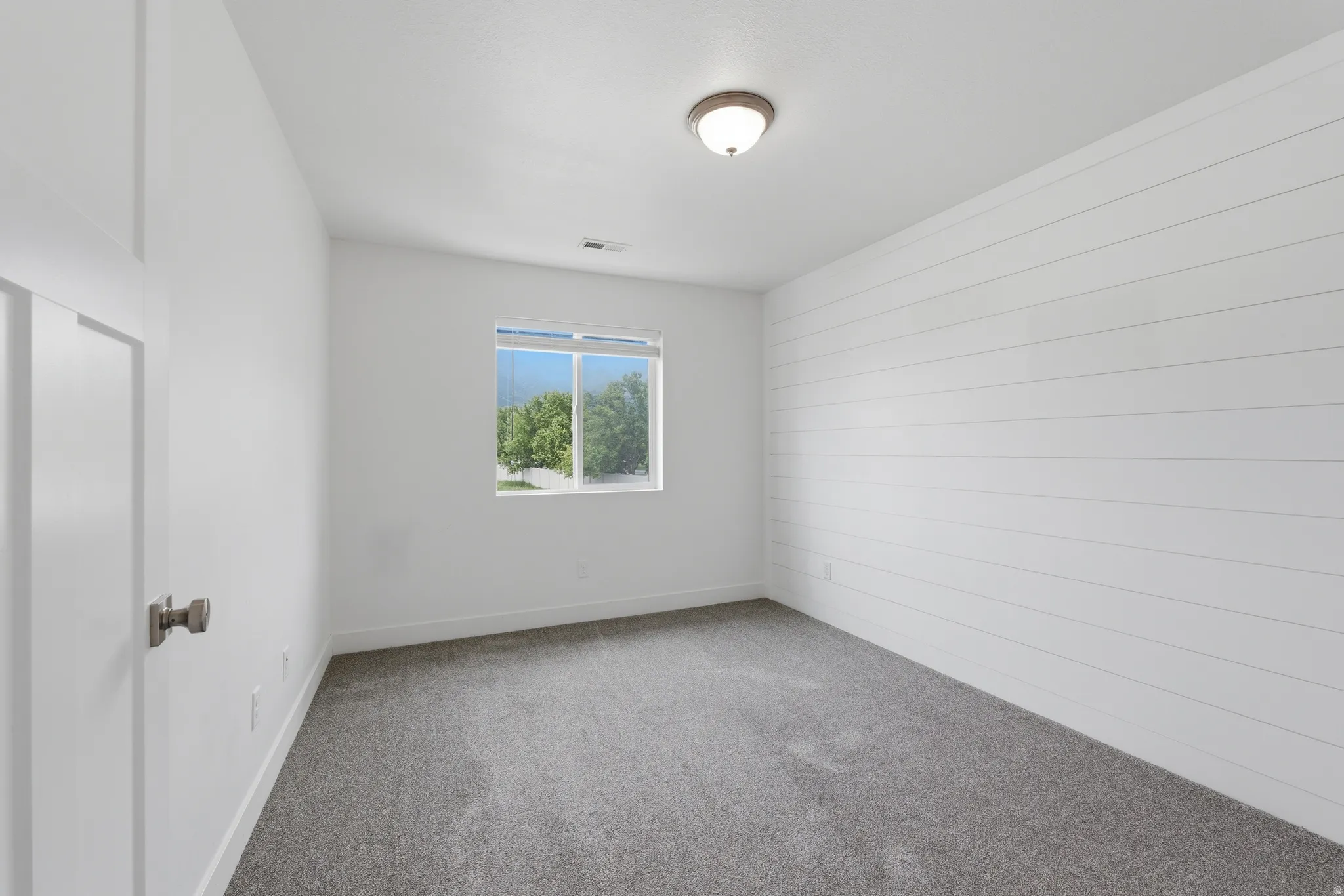 Bedroom featuring a shiplap accent wall, neutral carpeting, and a window providing natural light