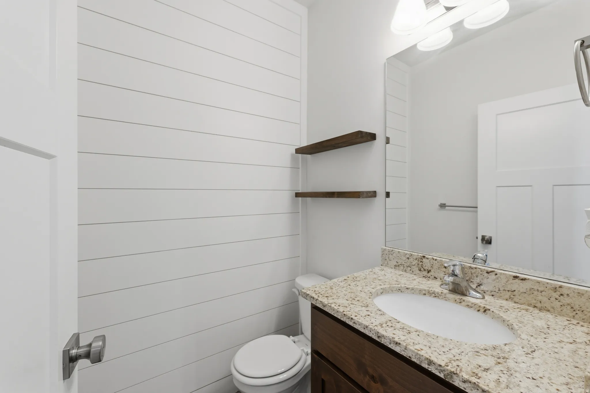 Bathroom featuring white shiplap walls, a vanity with a light-toned stone countertop, an integrated sink, and a dark wood-finish cabinet