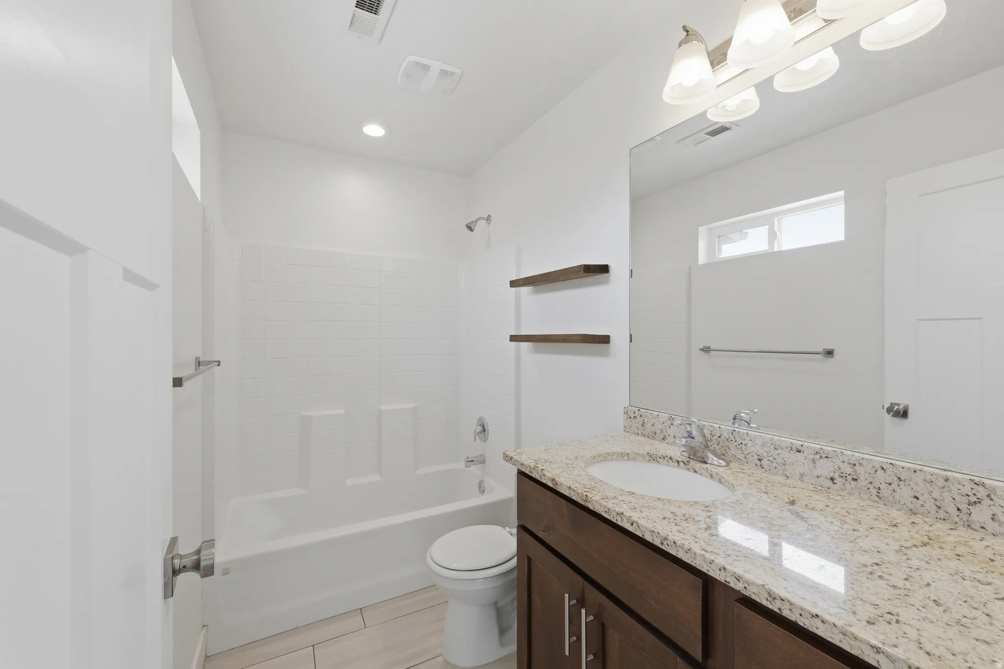 Bathroom featuring a vanity with a light granite countertop and undermount sink, dark wood-finish cabinetry, a full-width mirror, and a shower-tub combination with white subway tile surround