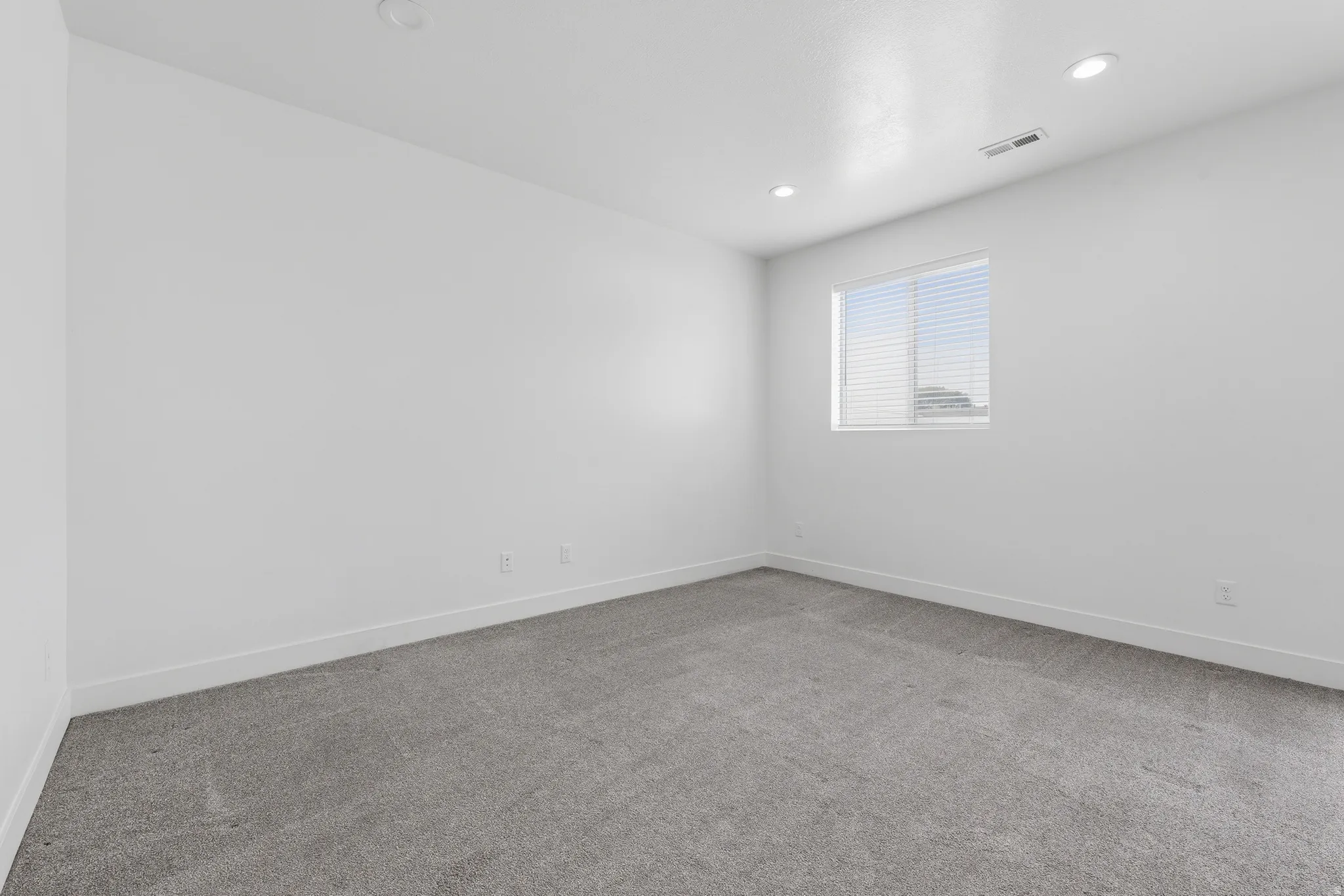 Room featuring neutral gray carpeting, white walls, recessed ceiling lighting, a single window with blinds, and white baseboards