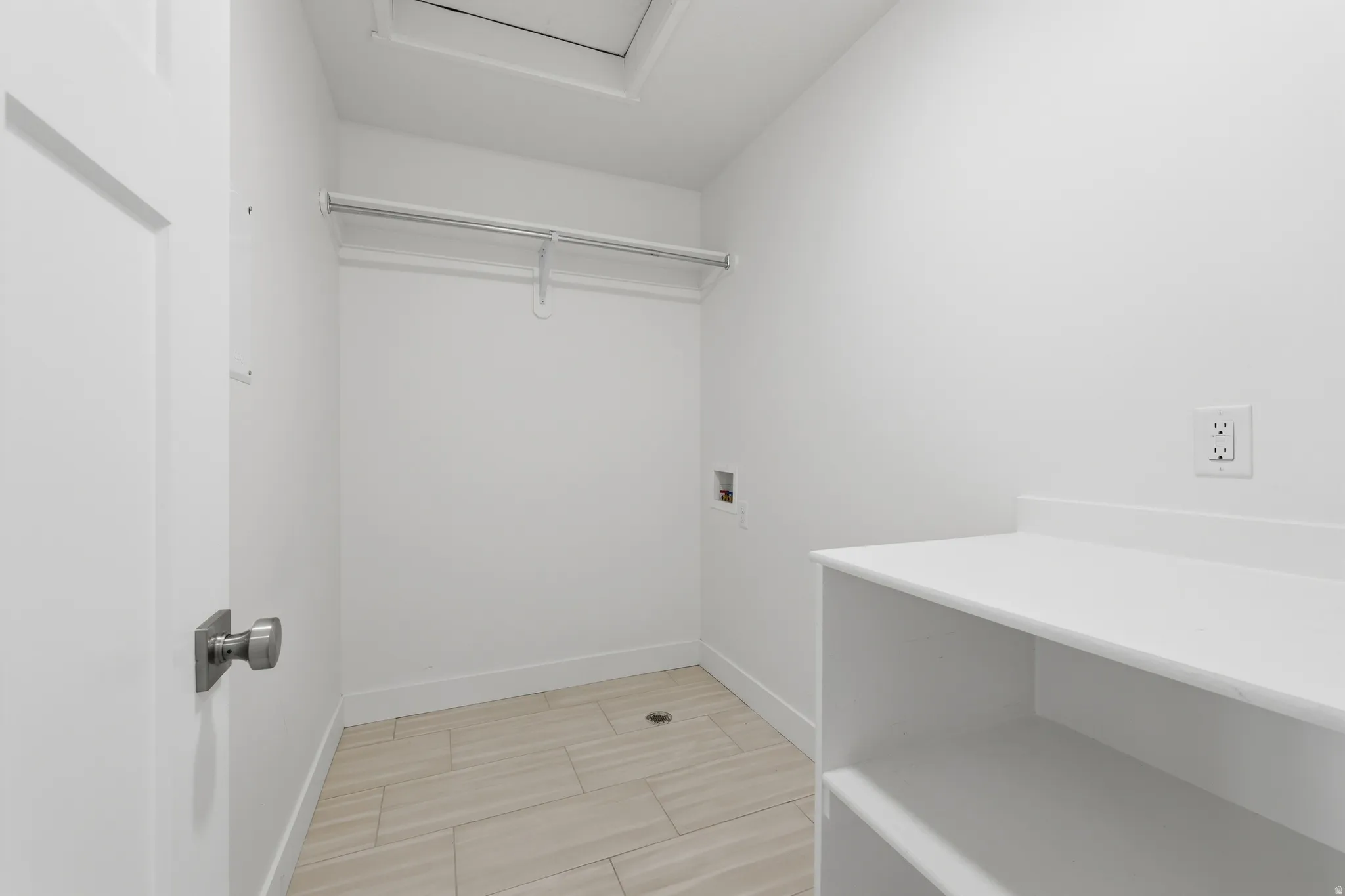 Bright utility space featuring light-toned wood-finish flooring, white walls, and built-in shelving