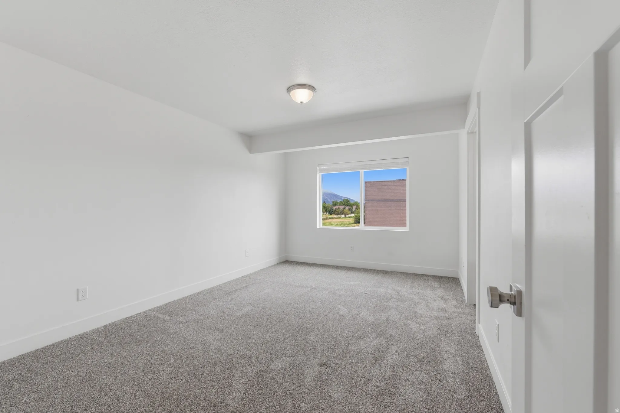 Spacious room with plush gray carpeting, white walls, and a large window offering natural light