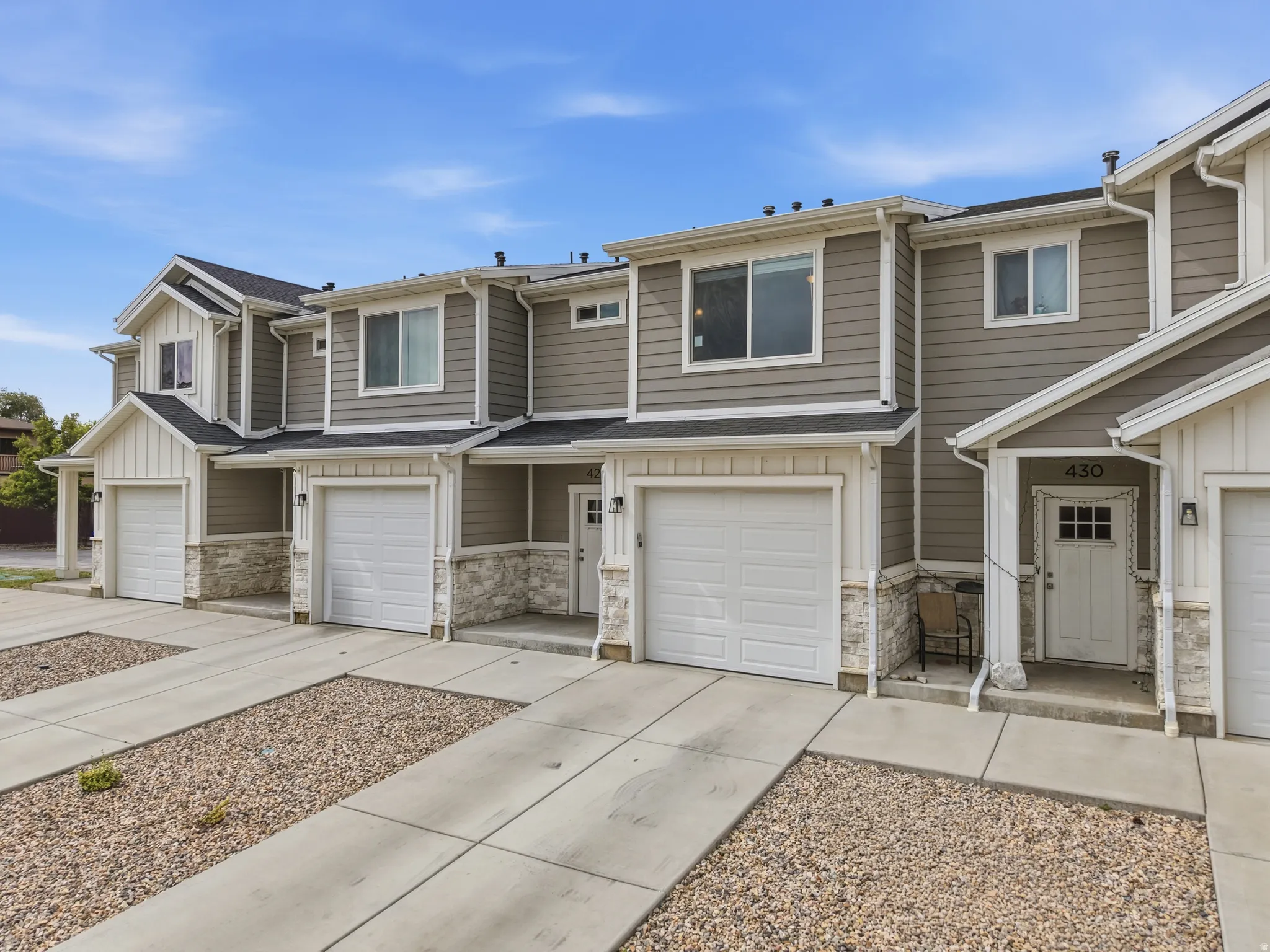 Multi-level townhome exterior featuring gray siding, white trim, stone veneer accents, and an attached two-car garage