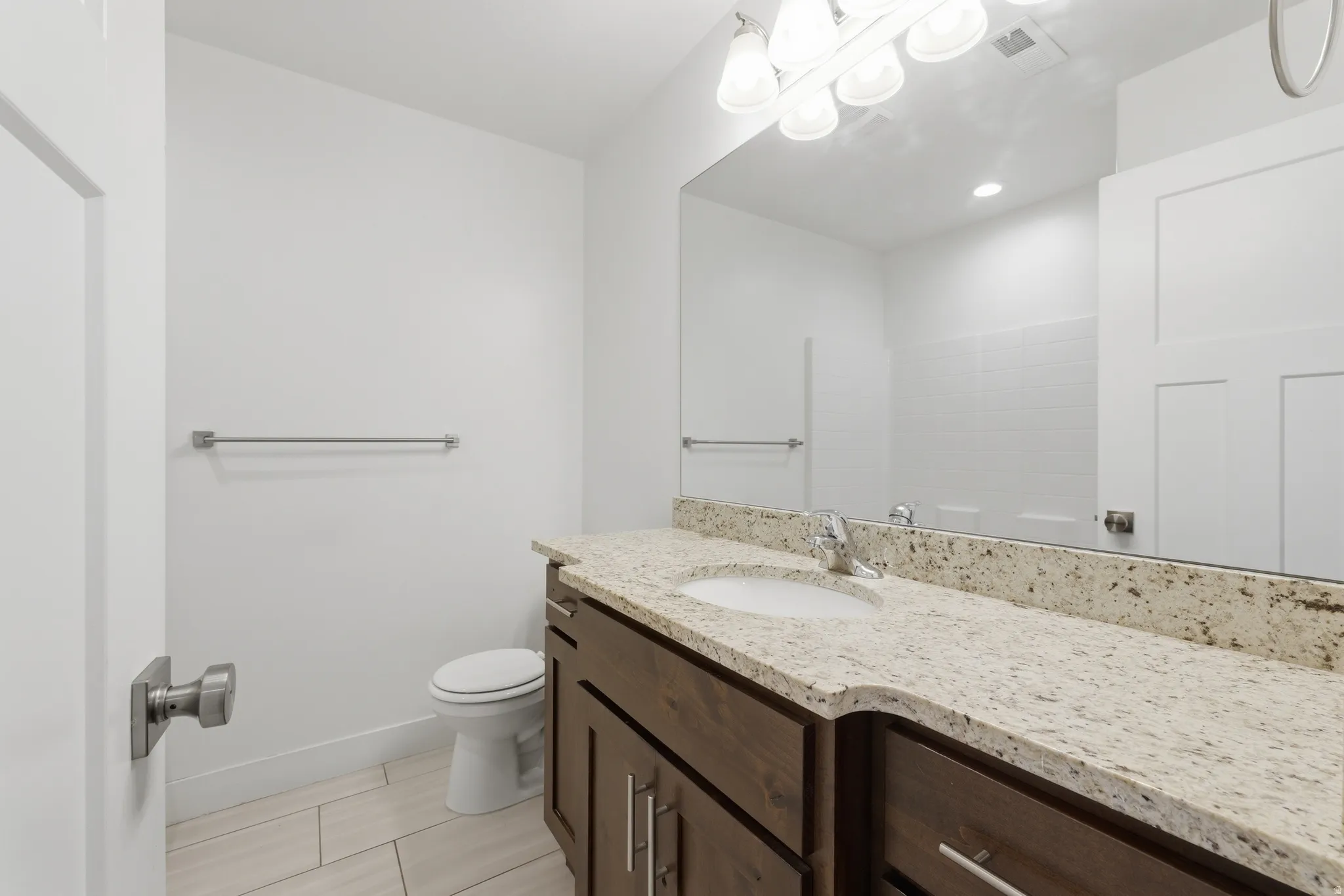 Bathroom featuring a wood-finish vanity with a light-toned countertop, a rectangular sink, and a large mirror