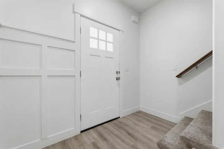 Entryway featuring a panel door with upper lites, board-and-batten wall detailing, wood-finish flooring, and a carpeted staircase with a wood handrail