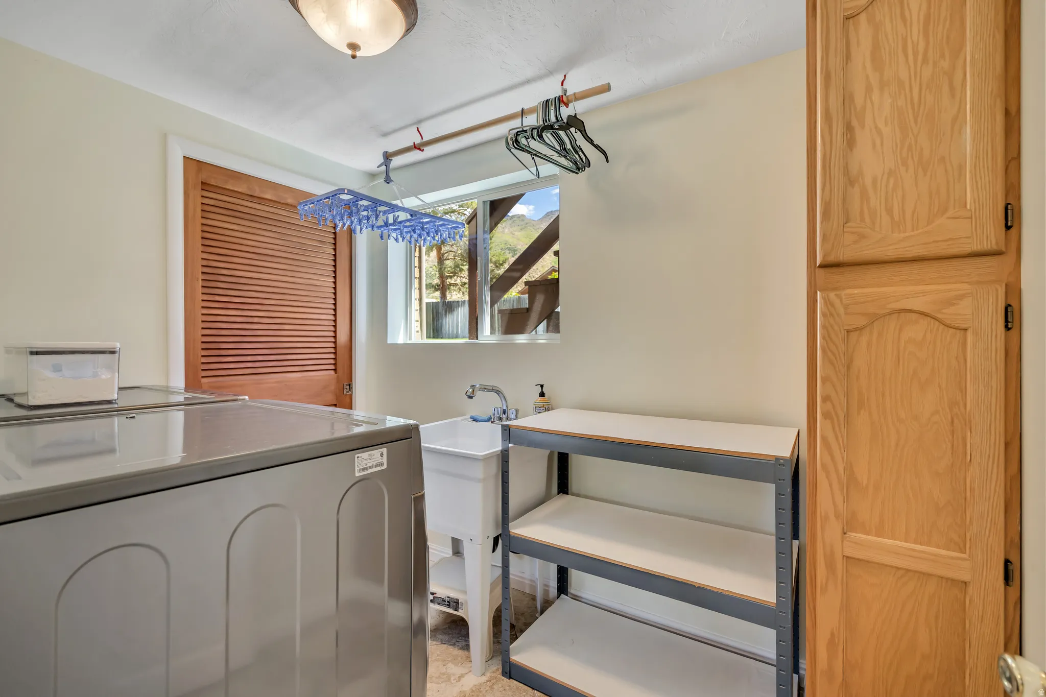 Utility room featuring a built-in wood cabinet, single basin utility sink, louvered wood door, and a ceiling-mounted light fixture