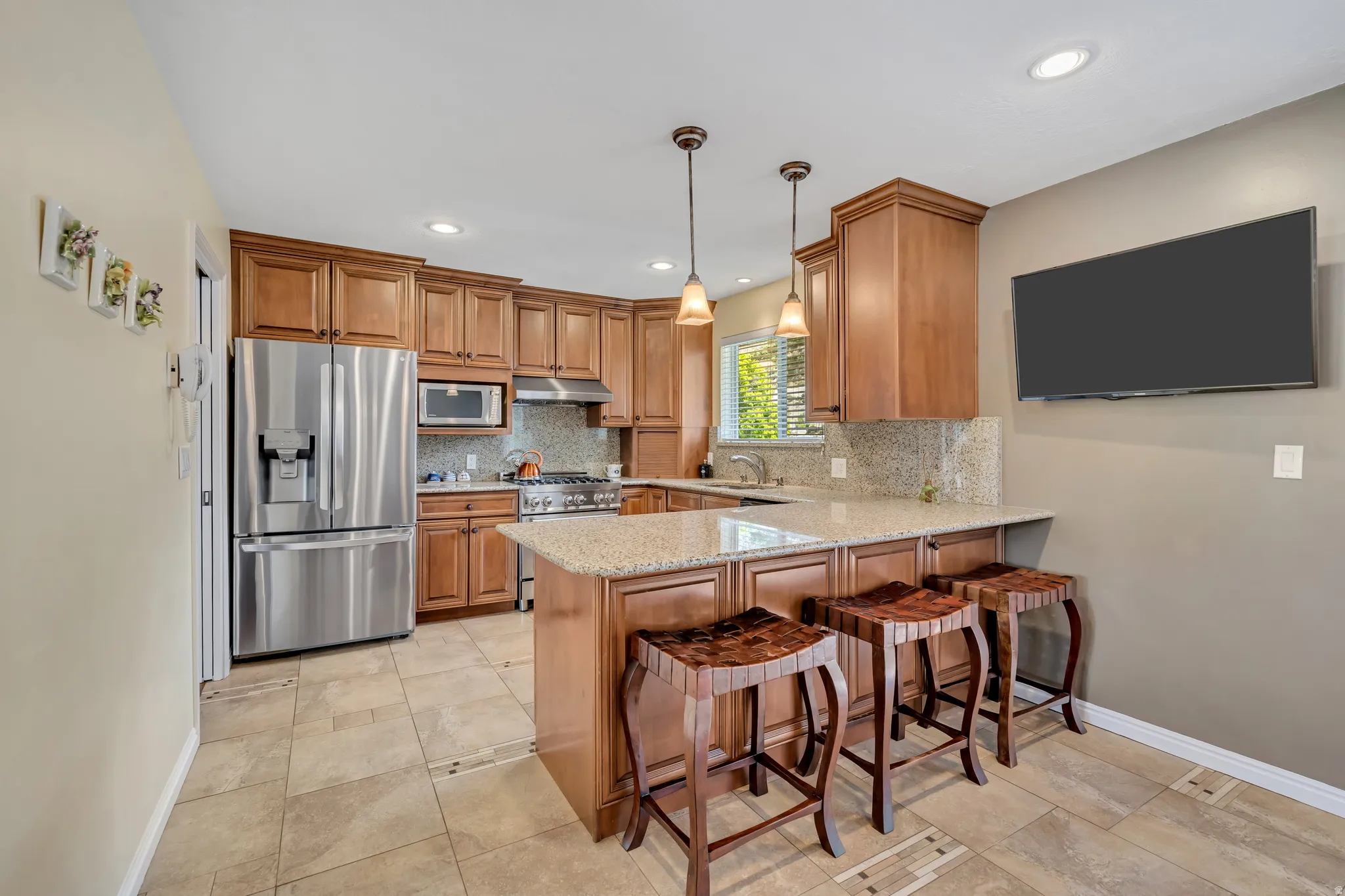 Kitchen featuring wood cabinetry, stainless steel appliances, a granite countertop island with pendant lighting, a tile backsplash, and tile flooring