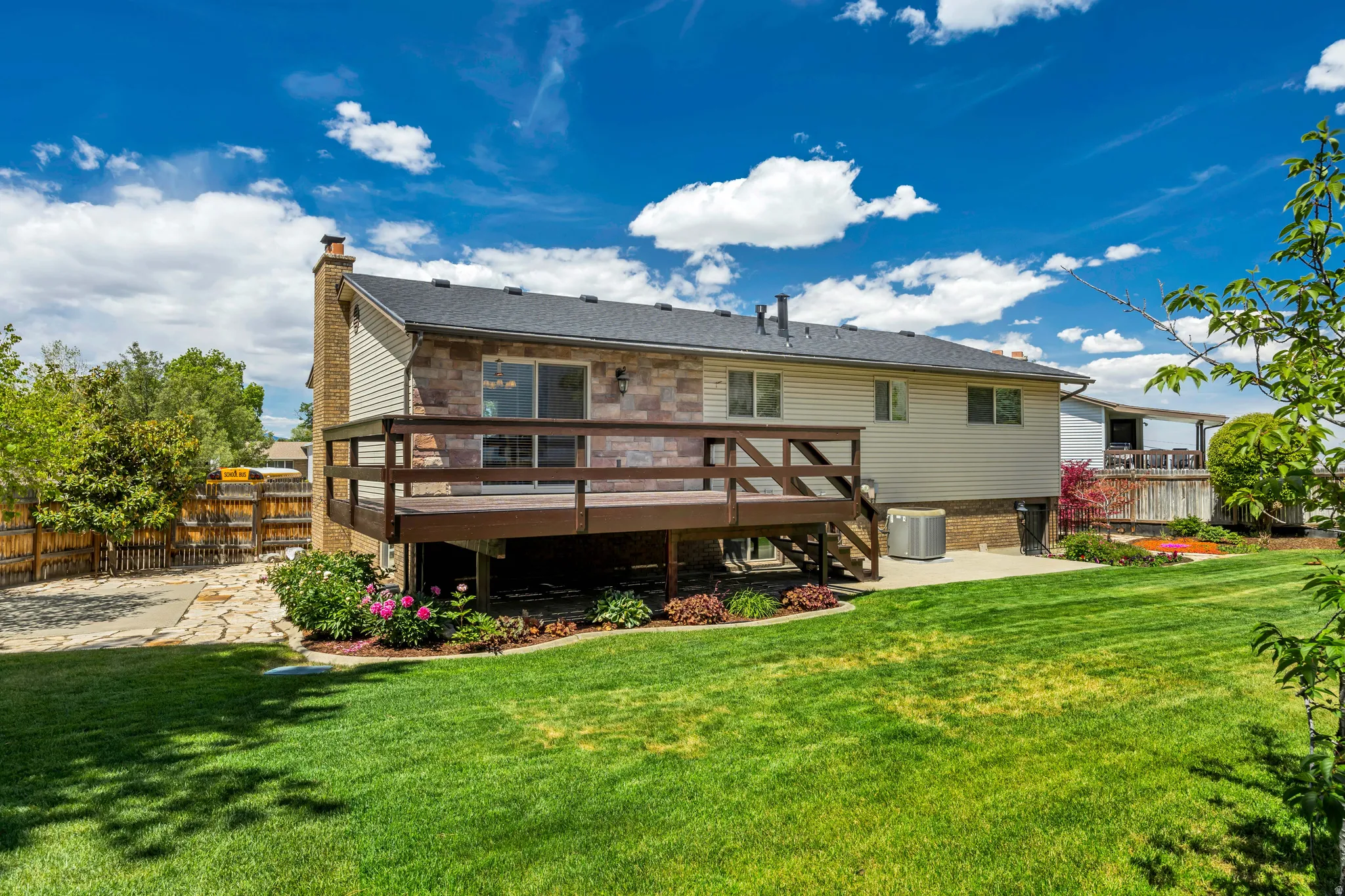 Expansive backyard featuring a manicured lawn, a two-story wood deck, and an adjacent stone patio