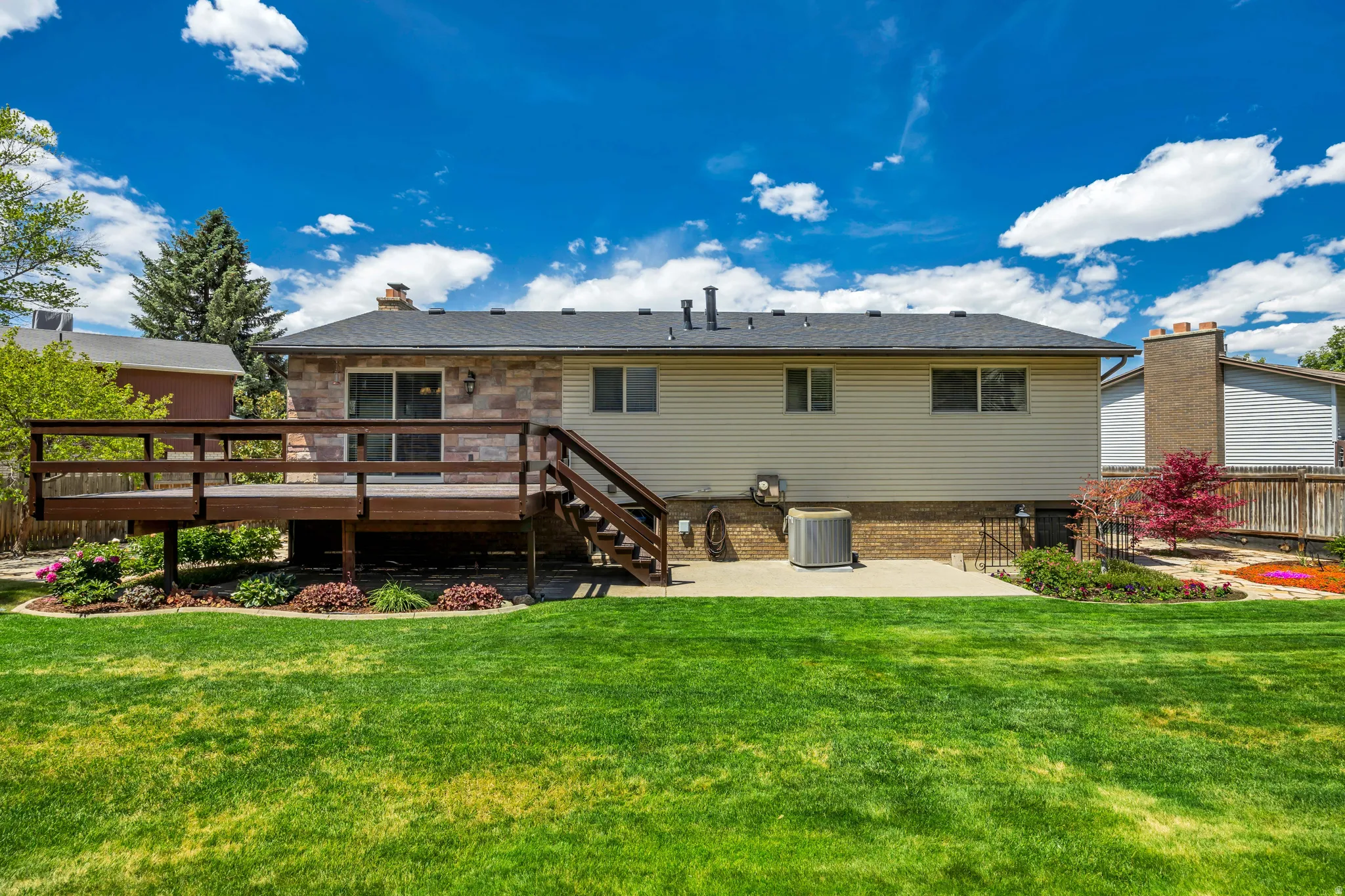 Expansive backyard featuring a manicured lawn, a large wood deck with steps, and a concrete patio
