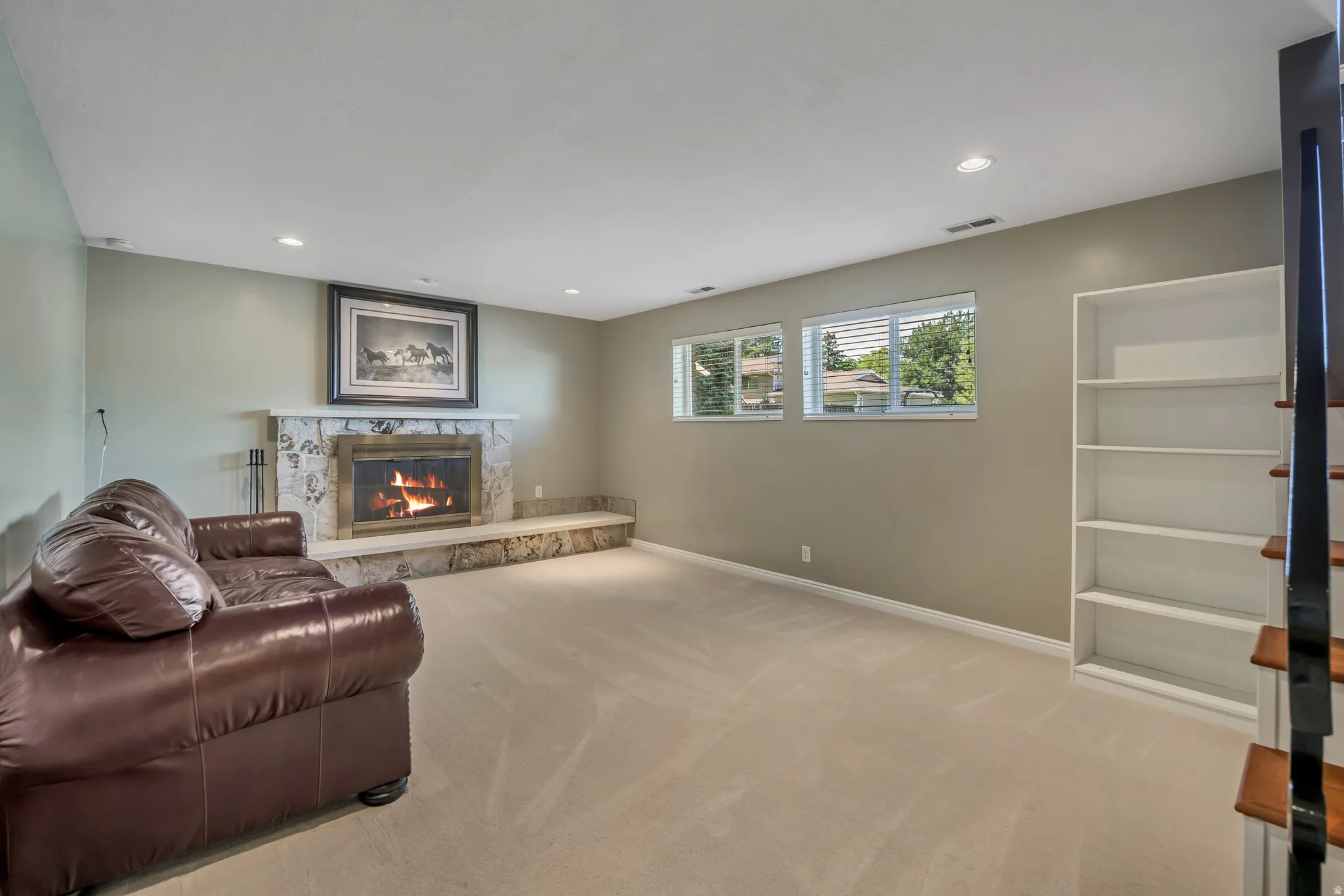 Spacious living area featuring a stone-clad fireplace with a hearth, recessed lighting, and light-colored carpeting