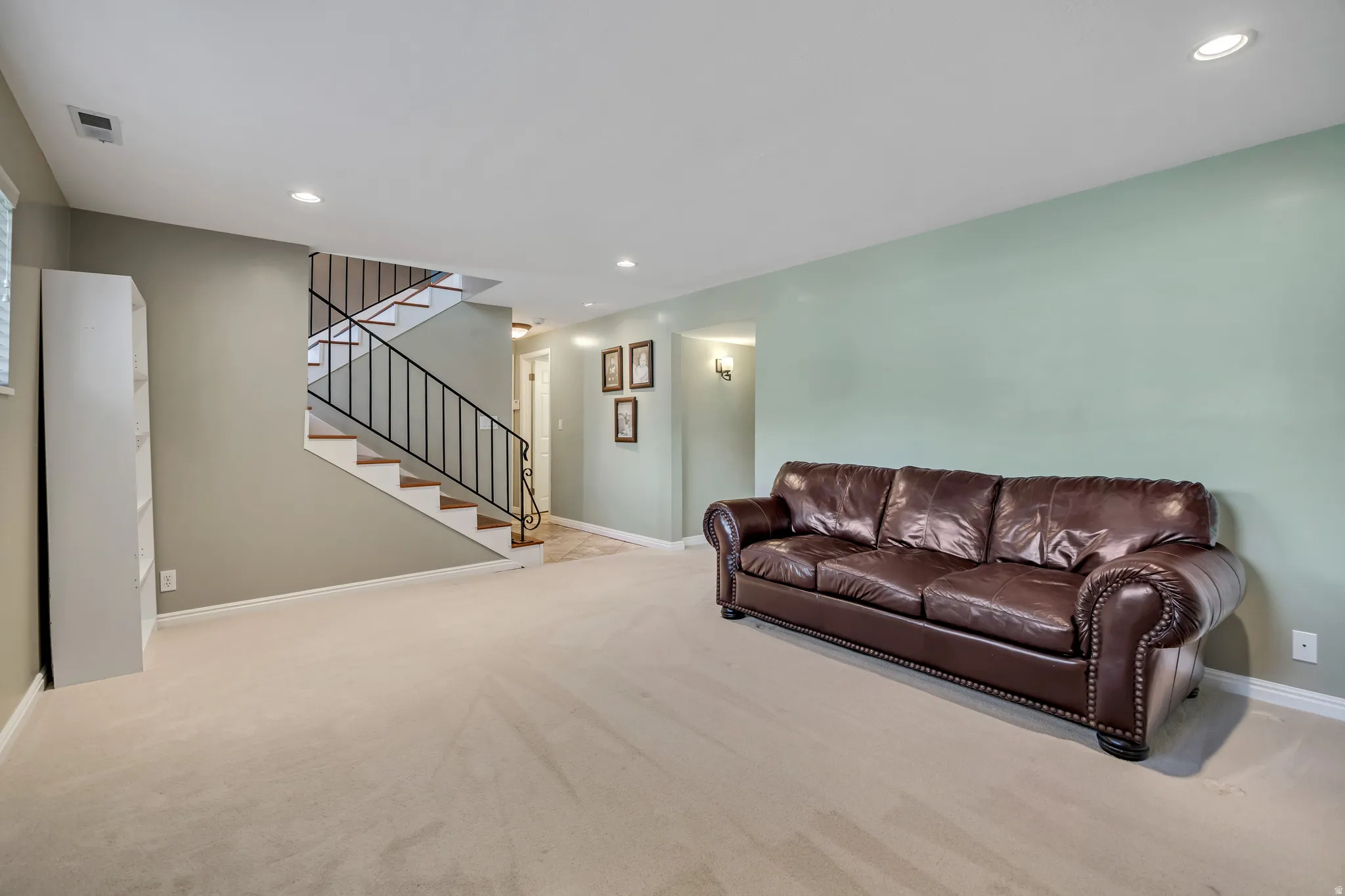 Spacious room featuring neutral carpet flooring, recessed lighting, and a staircase with open risers and black metal balusters