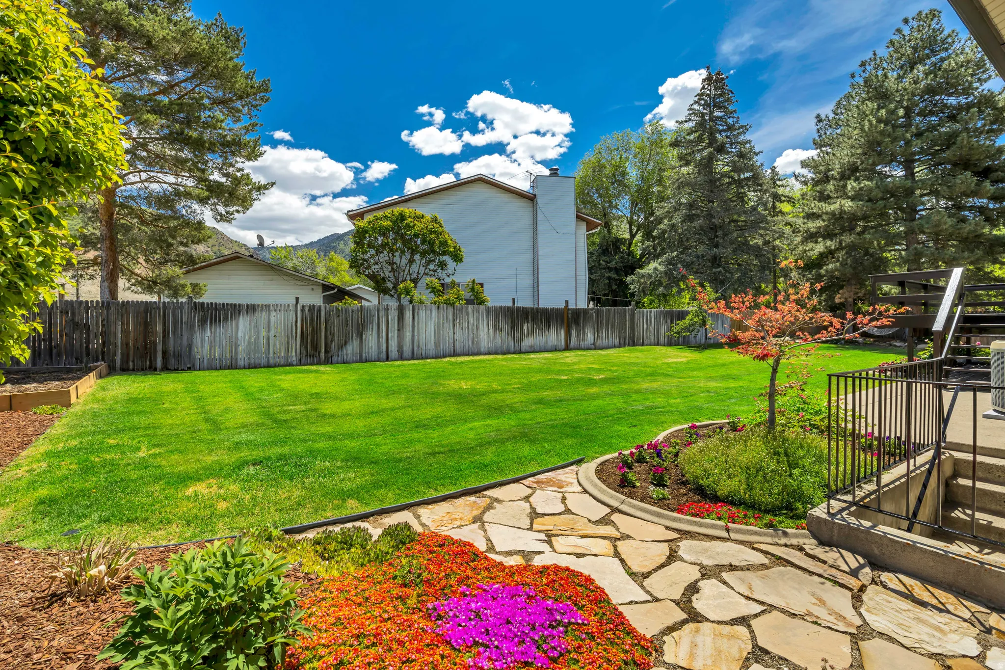 Expansive backyard featuring a manicured lawn, flagstone patio, and mature trees