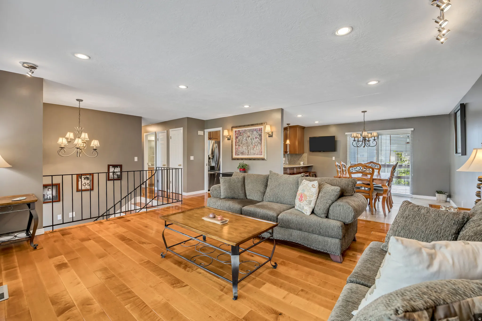 Open-concept living area featuring wood-finish flooring, recessed lighting, and a wrought iron railing