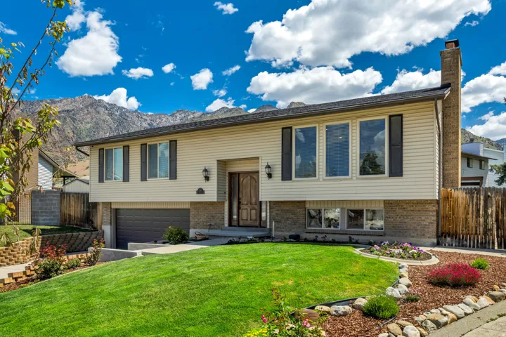Split-level residence featuring a two-car garage, brick and siding exterior, large front windows, and a landscaped yard with rock accents