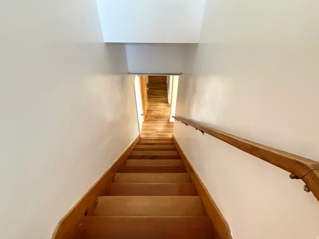 Wood-finish staircase with a matching wood handrail, light-colored walls, and a recessed ceiling element