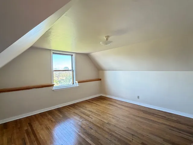 Attic room featuring sloped ceilings, hardwood flooring, and a single-pane window