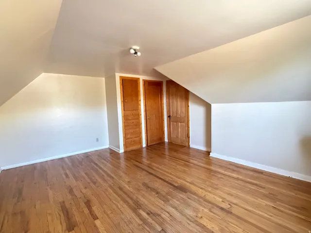 Attic space featuring wood-finish flooring, white walls, and a sloped ceiling