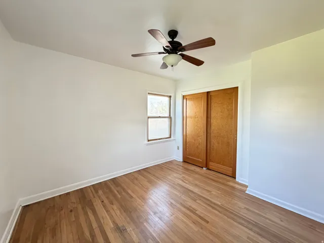 Room featuring wood-finish flooring, a ceiling fan with integrated lighting, a double-pane window, and a built-in closet with sliding wood doors
