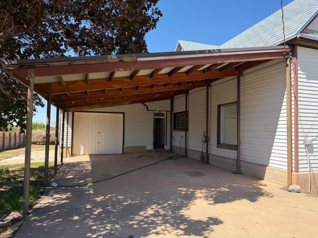 Covered carport with a concrete slab, attached to a property featuring horizontal siding and multiple windows