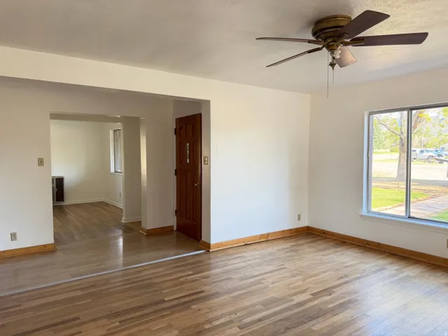 Spacious living area featuring wood-finish flooring, a ceiling fan, and ample natural light from a large window