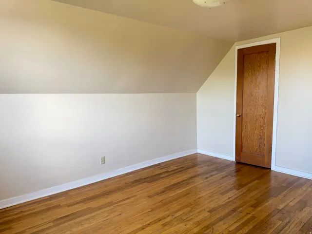 Room featuring wood-finish flooring, a solid wood door with brass hardware, and painted walls with white trim