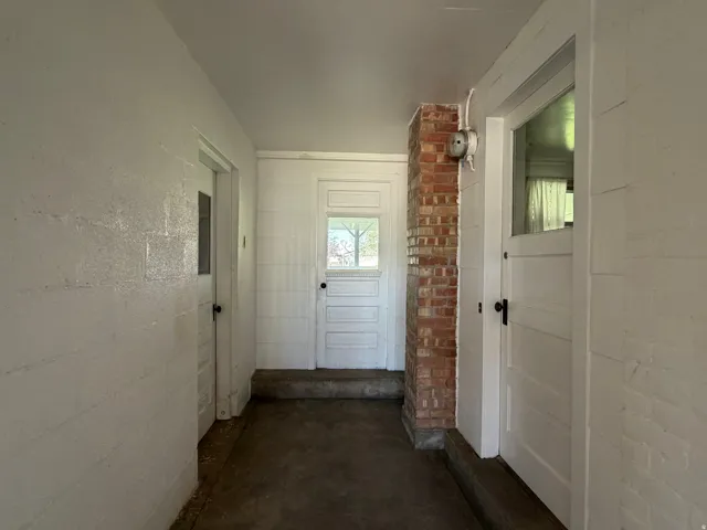 Breezeway to garage from mud room. Interior hallway featuring white painted brick walls and a partial exposed brick column