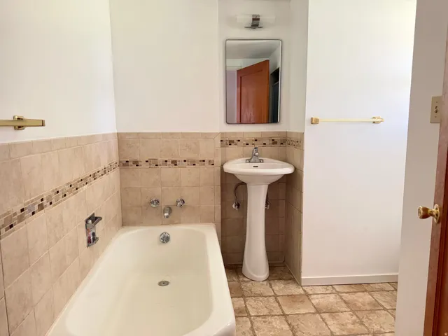 Bathroom featuring a pedestal sink, white bathtub, rectangular vanity mirror, and polished chrome fixtures